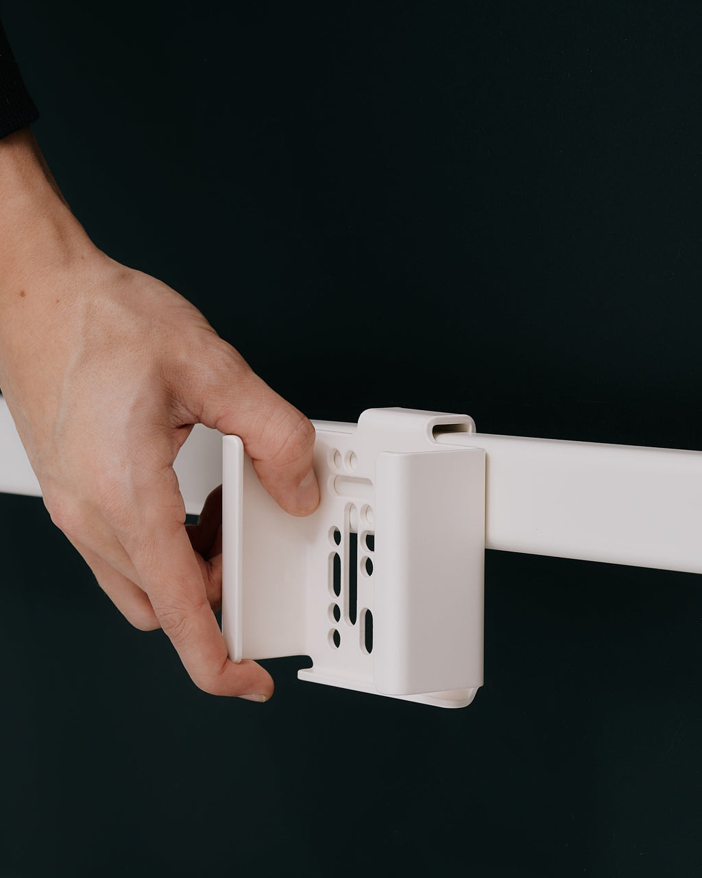 Hand sliding the white Apple TV 4K Mount onto a rail, close-up detail shot against a mossy green studio backdrop