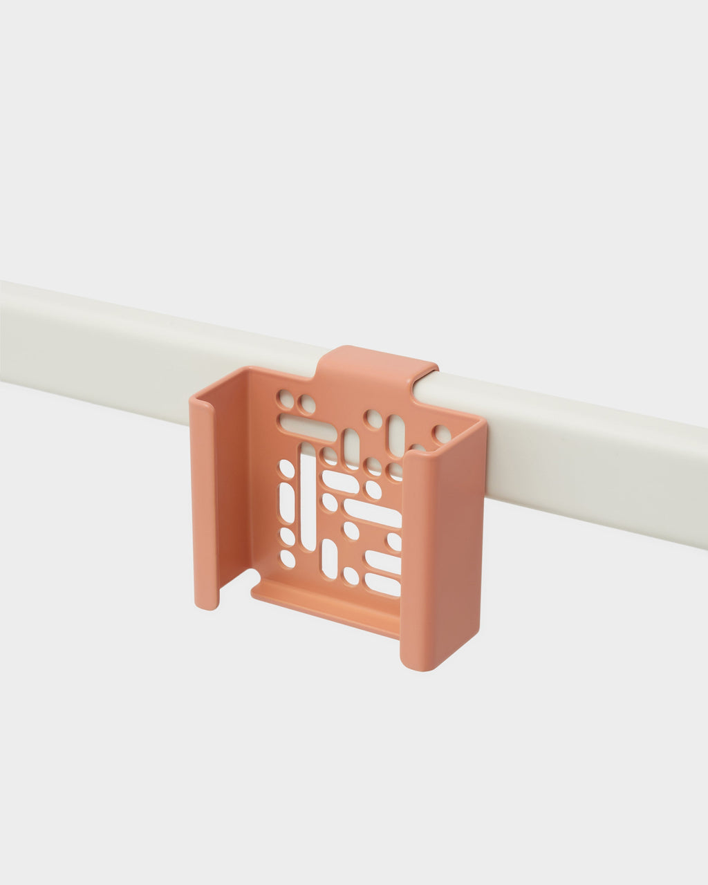 Dusty Rose Apple TV Mount hooked over a white rail in a studio packshot, angled view showing perforated back panel