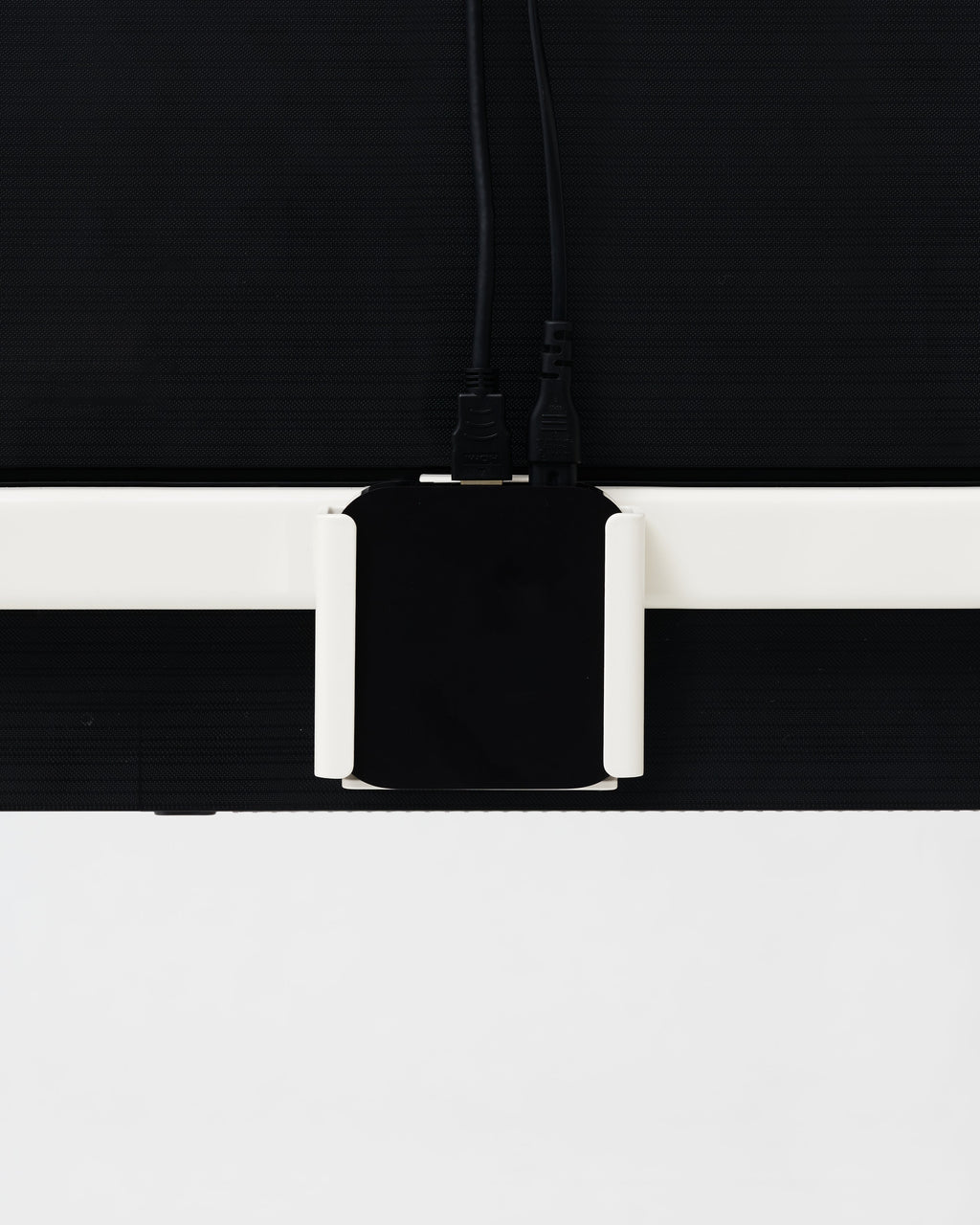 Oat Apple TV Mount holding a black Apple TV behind a wall-mounted TV, close-up rear view with HDMI and power cables