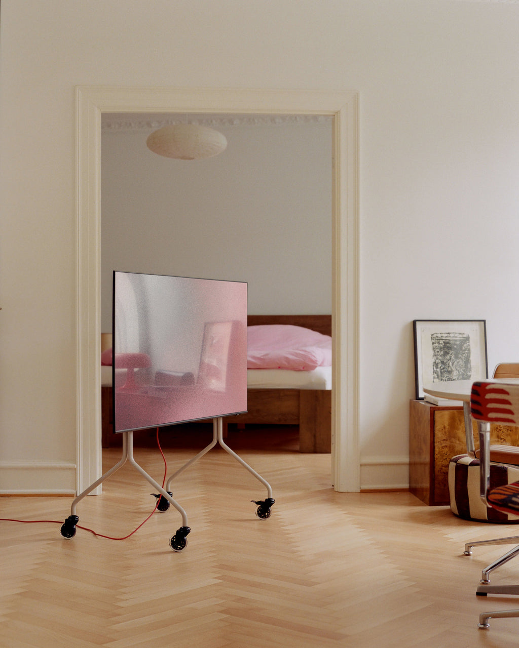 Blade Wheels in Black on a white TV floor stand rolling across herringbone parquet in a sunlit apartment doorway