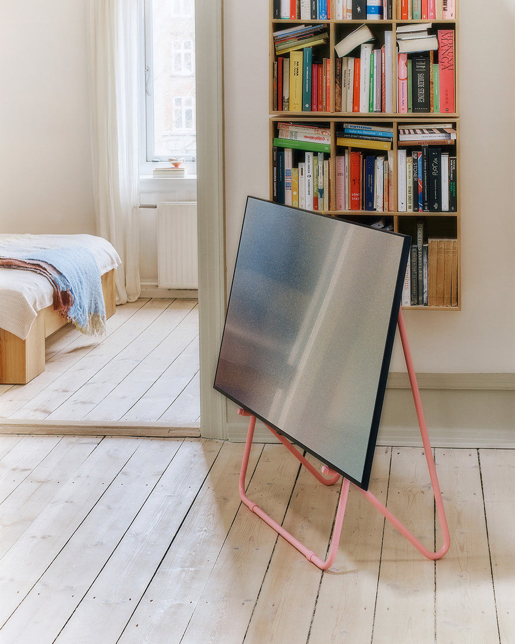 Bloom in Bubble Gum low TV stand holding a flatscreen in a bright bedroom with wood floors and a book-filled shelf