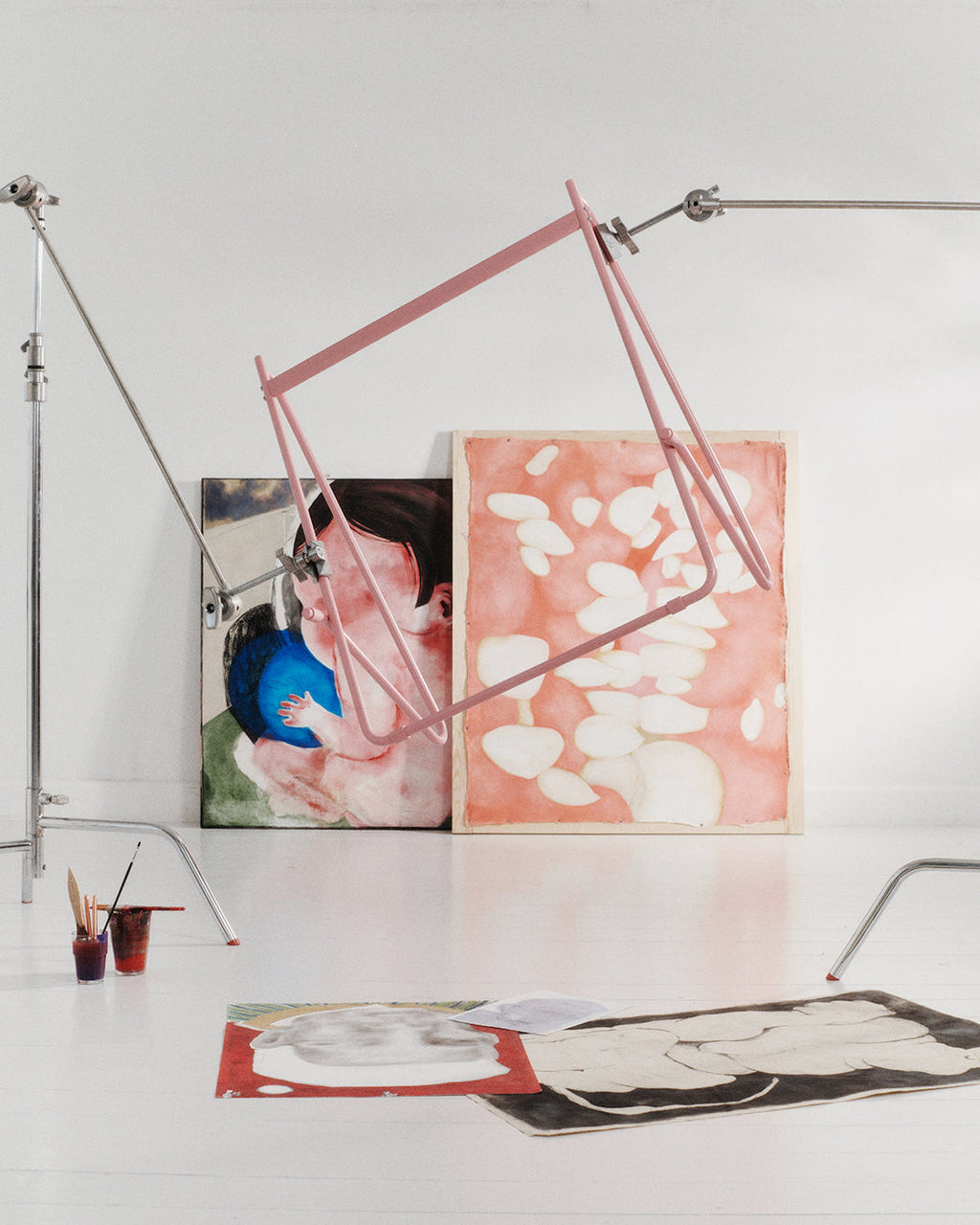 Bloom in Bubble Gum (Stands Low) pink frame suspended in a white artist studio above leaning paintings and artwork