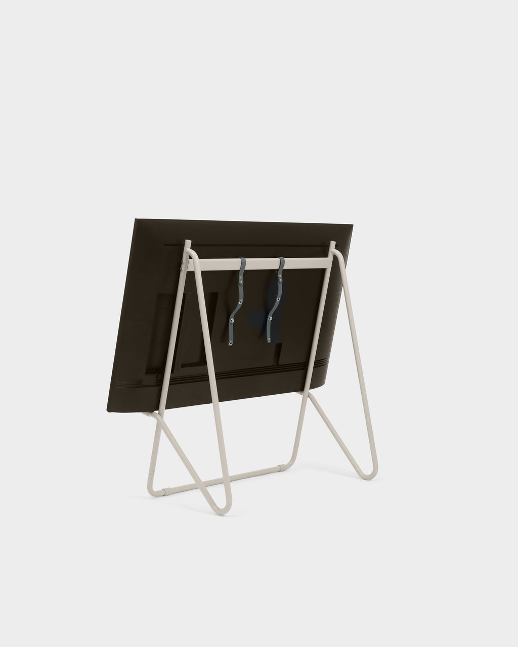 Rear three-quarter view of Bloom in Oat low stand holding a TV with leather straps, on a light studio backdrop