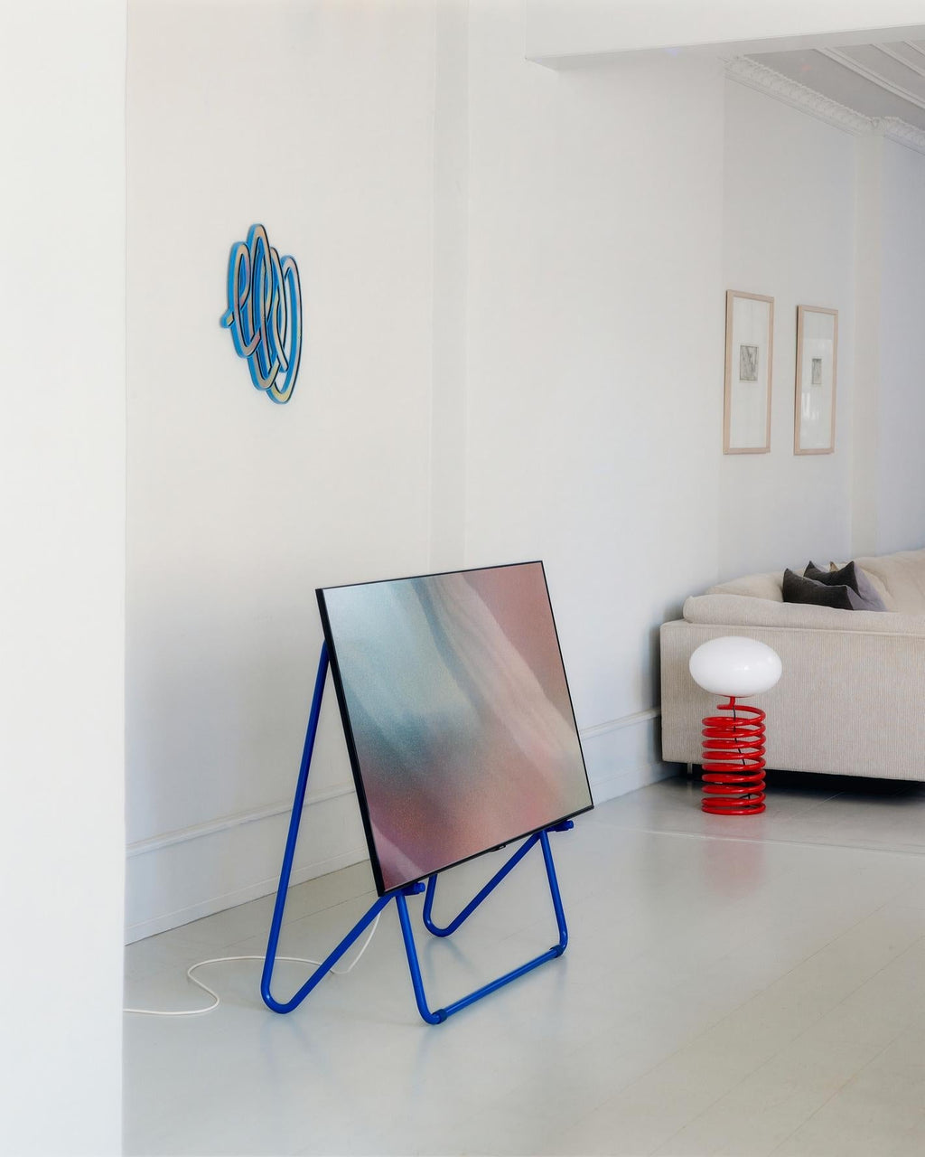 Bloom in Oat (Stands Low) blue tubular easel stand holding a screen in a bright white living room corner