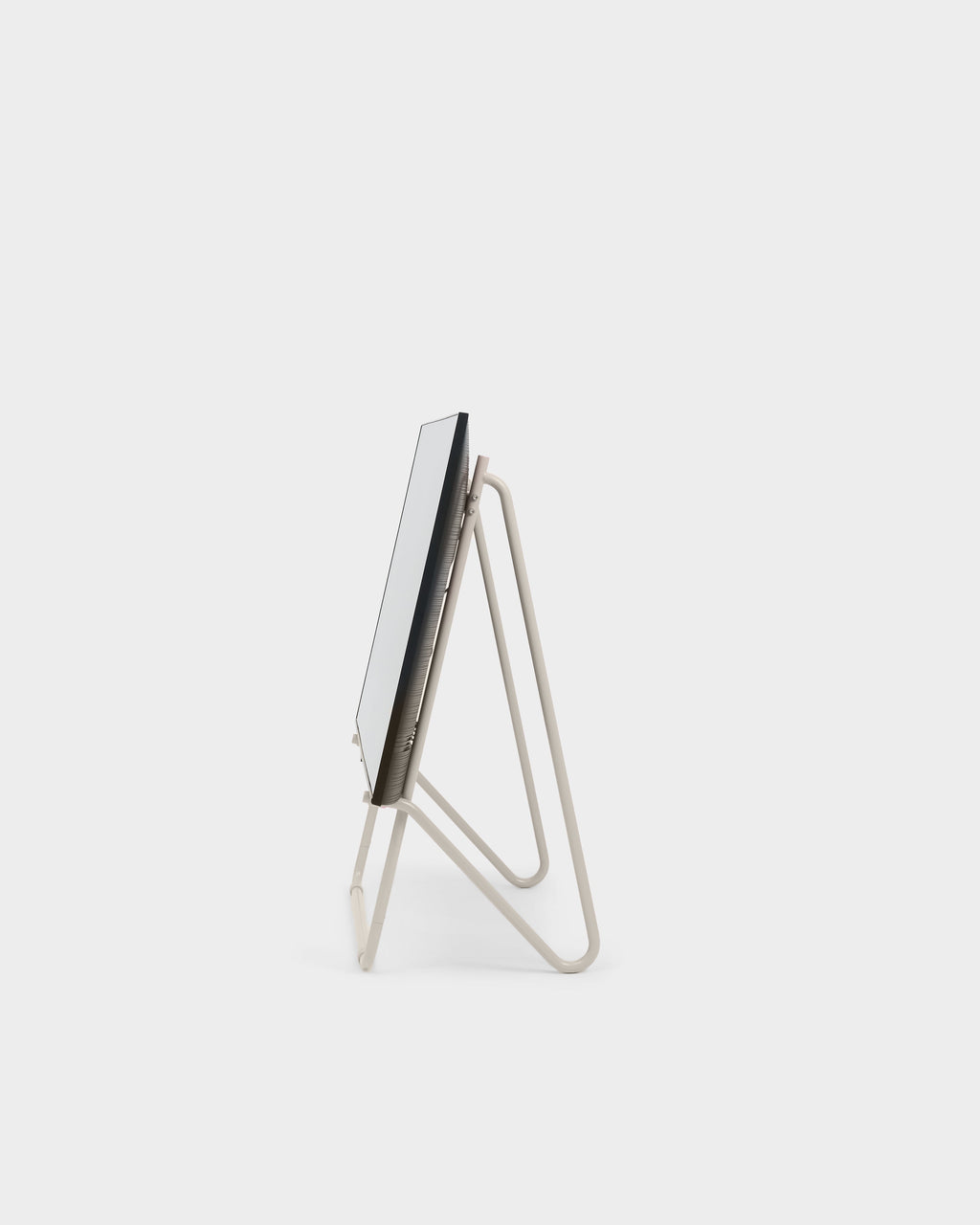 Side profile of Bloom in Oat low stand holding a flat screen on a light studio background, showing looped tube legs
