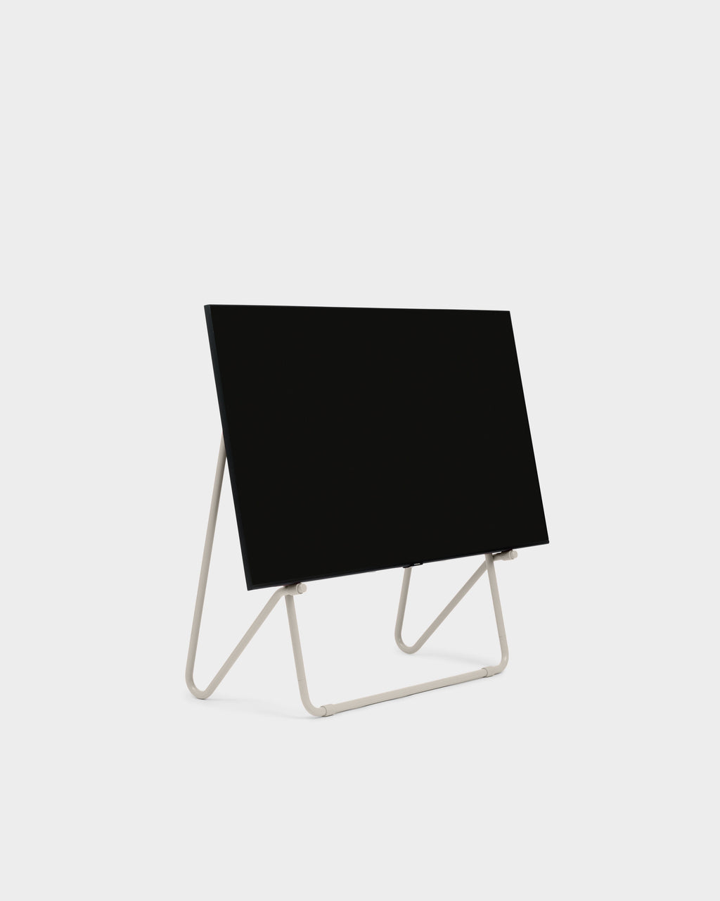 Bloom stand in Oat holding a black flat-screen TV, angled studio packshot on light grey with low tubular legs