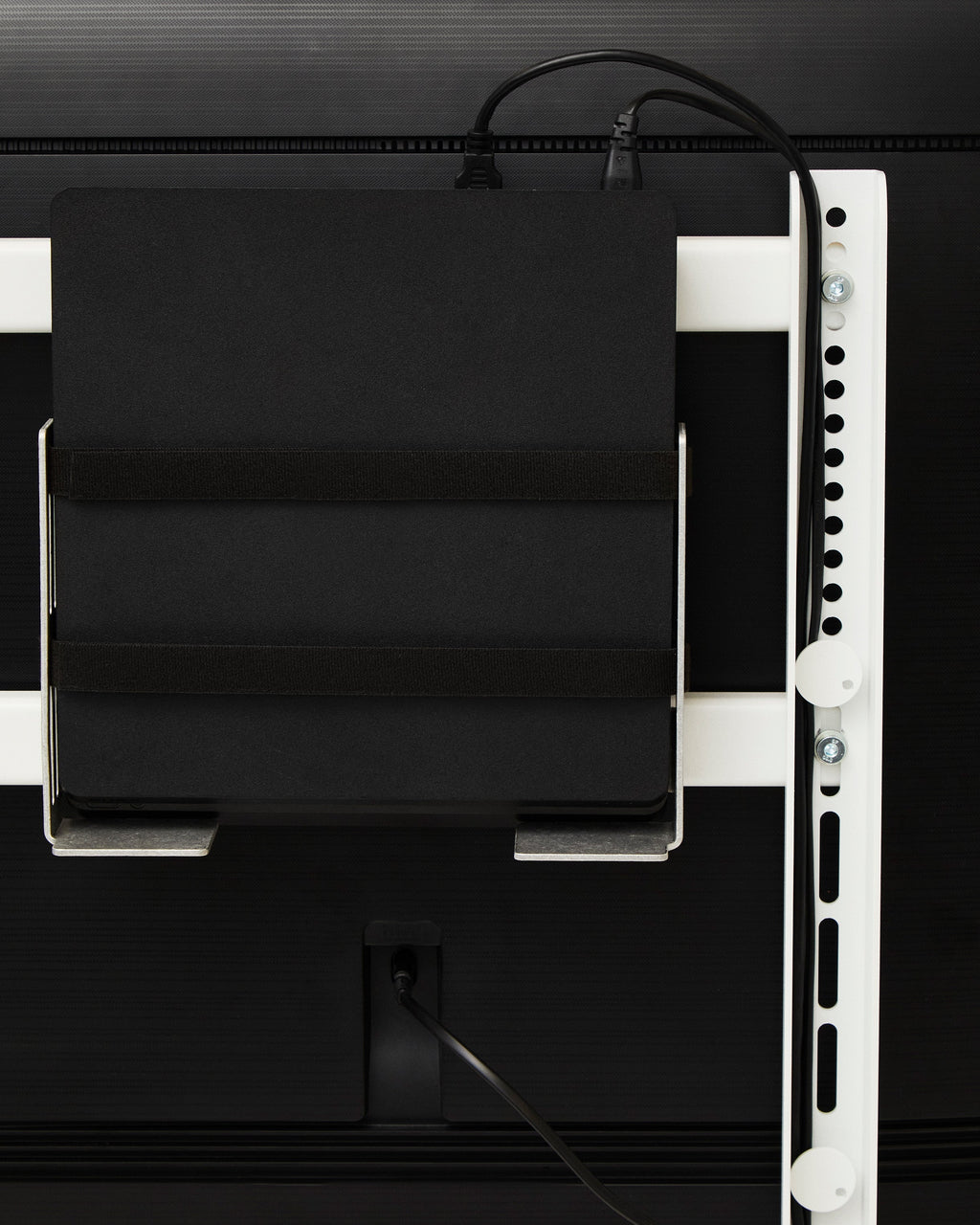 Oat Box Mount holding a black media device with hook-and-loop straps, bolted to a white wall channel behind a TV