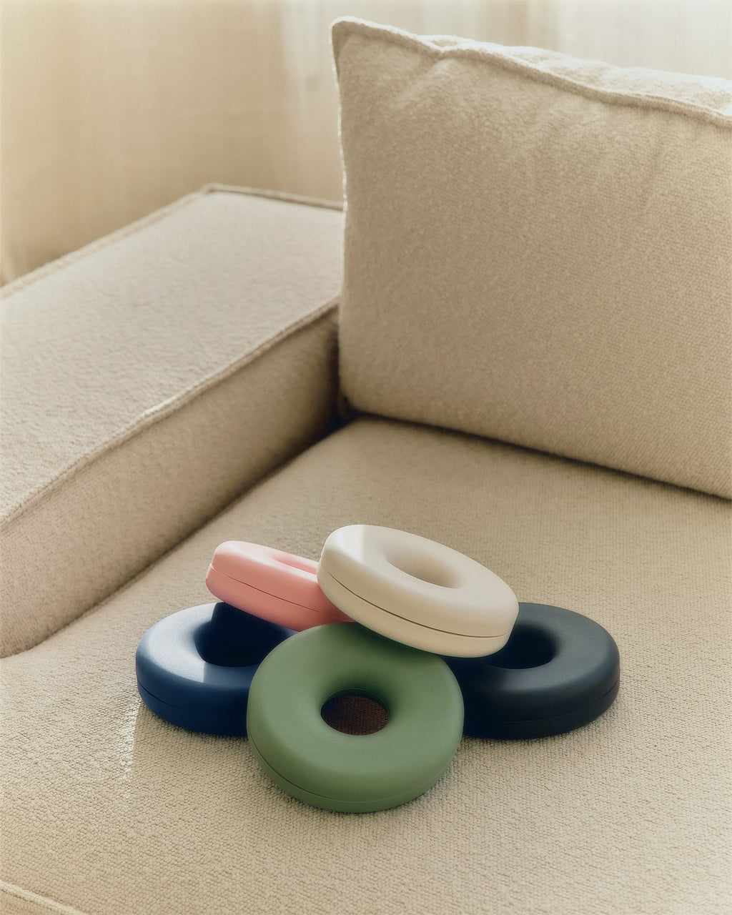 Pearl Cable Bagel resting atop pink, navy, black and green cable managers on a cream bouclé sofa