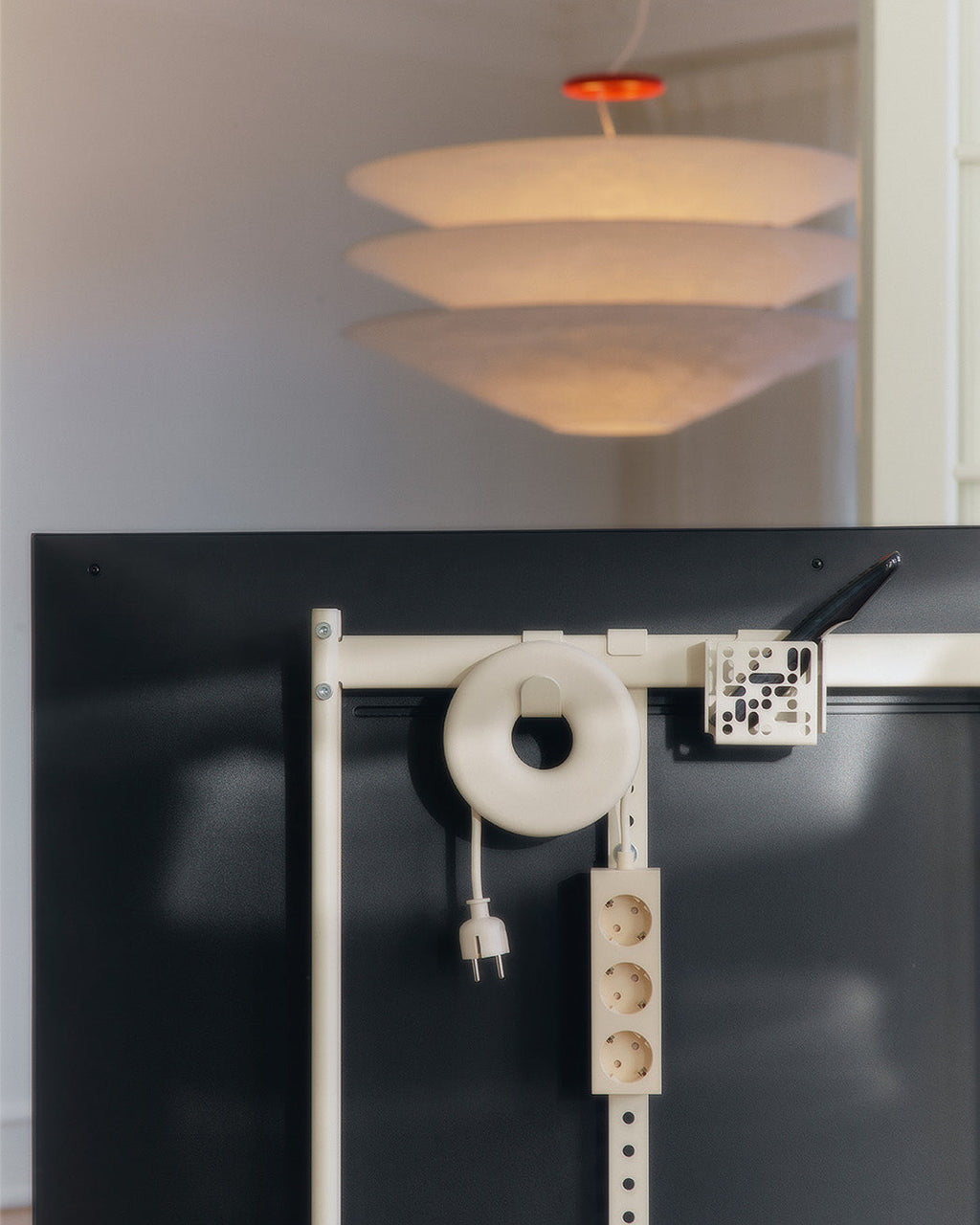 Pearl Cable Bagel coiling a white cable on a black desk-back rail with power strip, pendant lamp glowing above