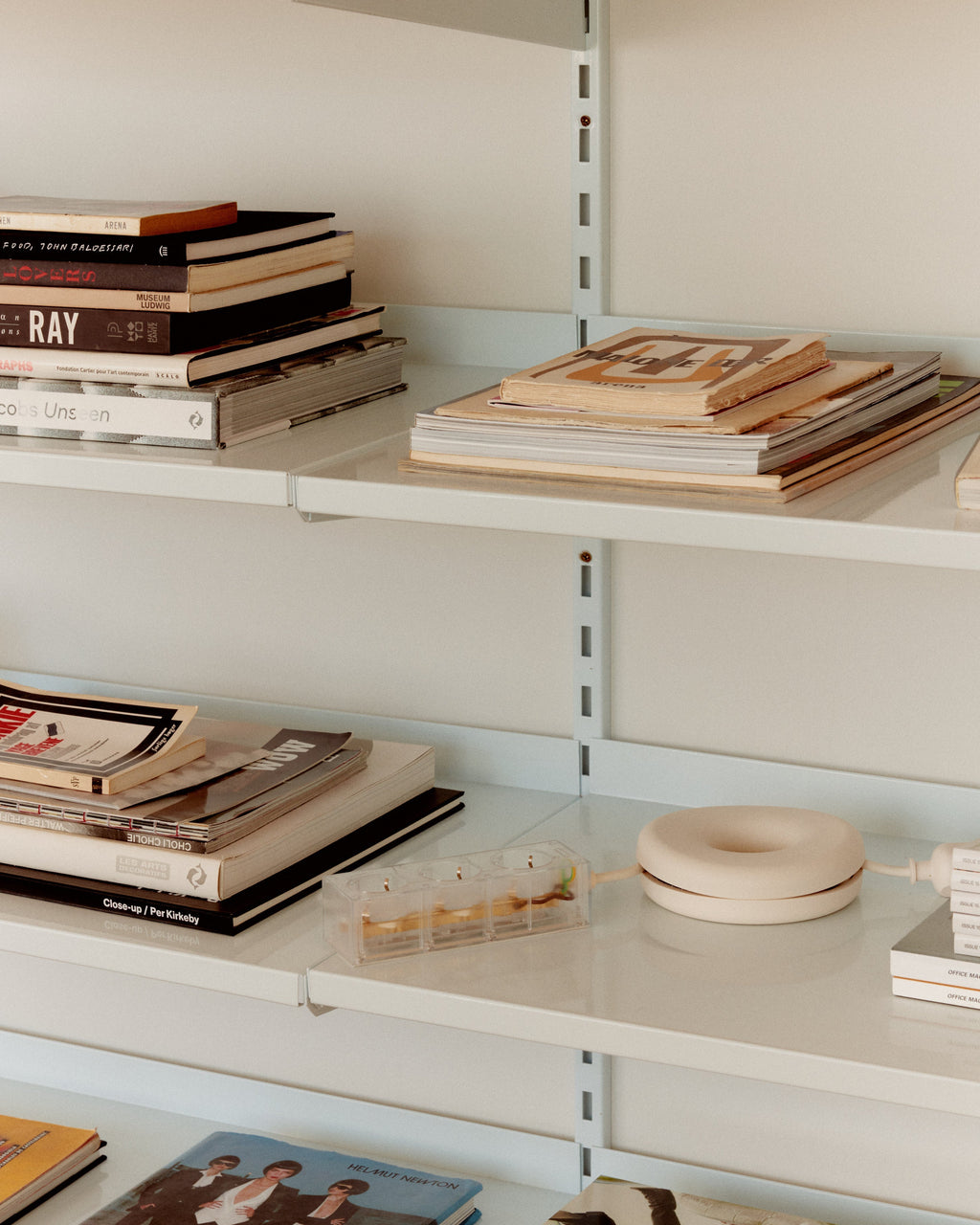 Pearl Cable Bagel coiling a power cord on a white shelf beside art books and a clear power strip