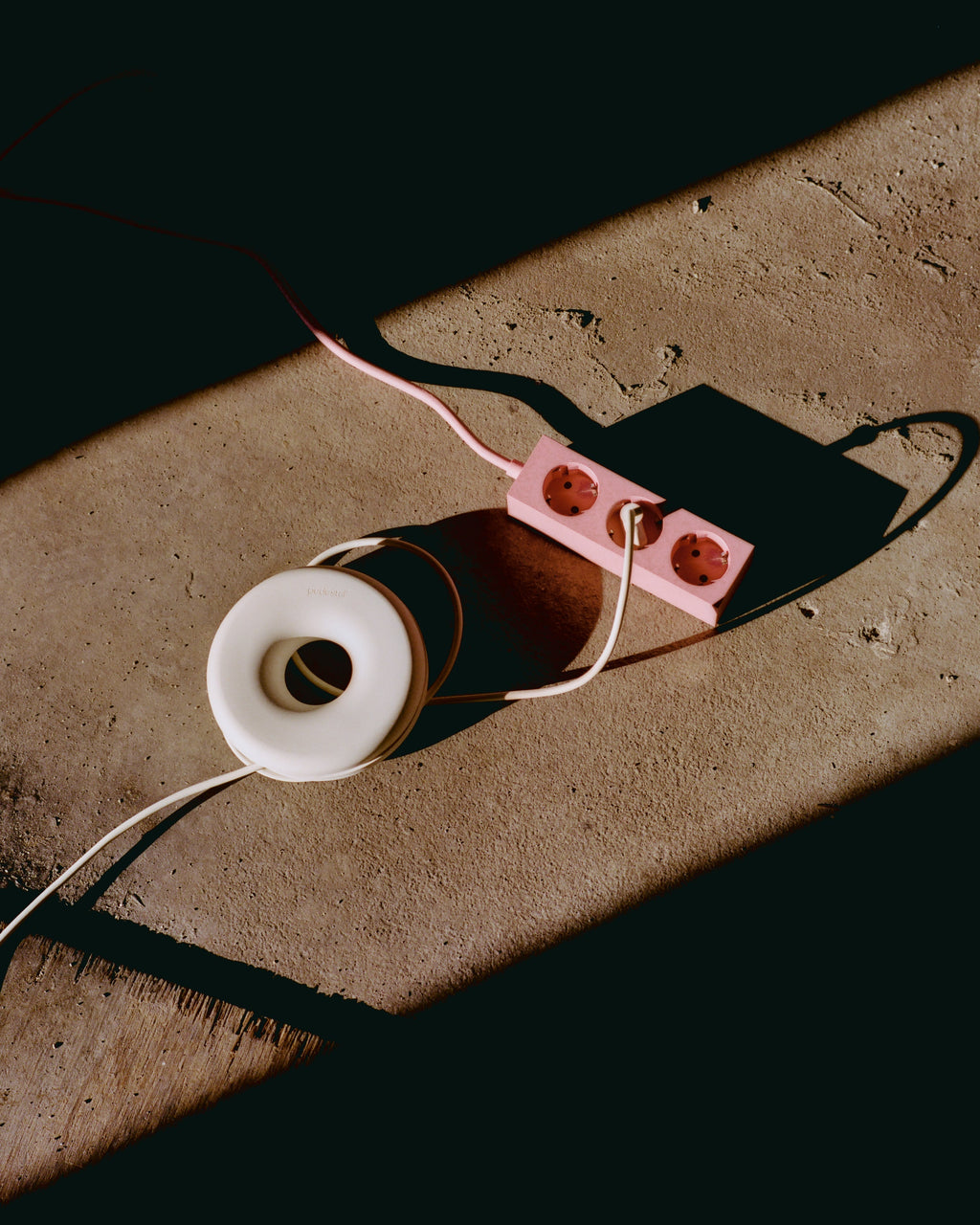 Pearl Cable Bagel coiling a white cord on sunlit concrete beside a pink power strip, overhead lifestyle angle