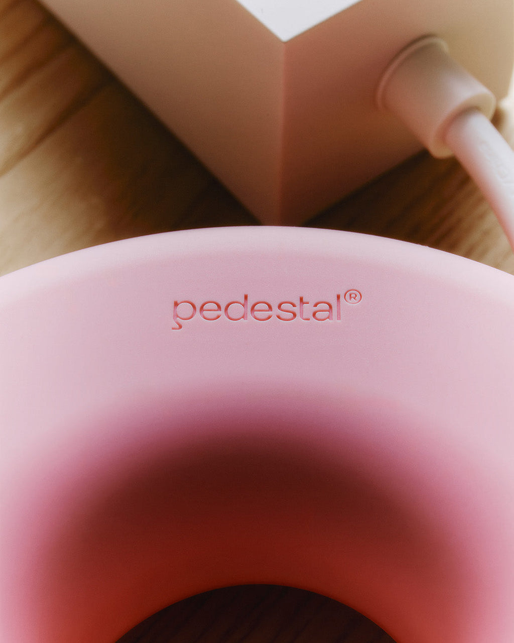 Close-up of the Cable Bagel in Bubble Gum showing embossed pedestal logo, with pink cable and packaging on a wood floor