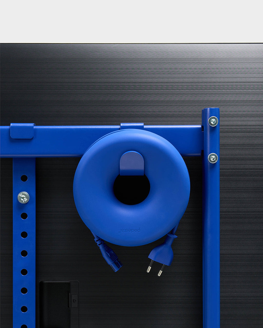Cable Bagel cable manager in blue mounted on a stand's crossbar, coiled power cord with EU plug hanging behind a TV