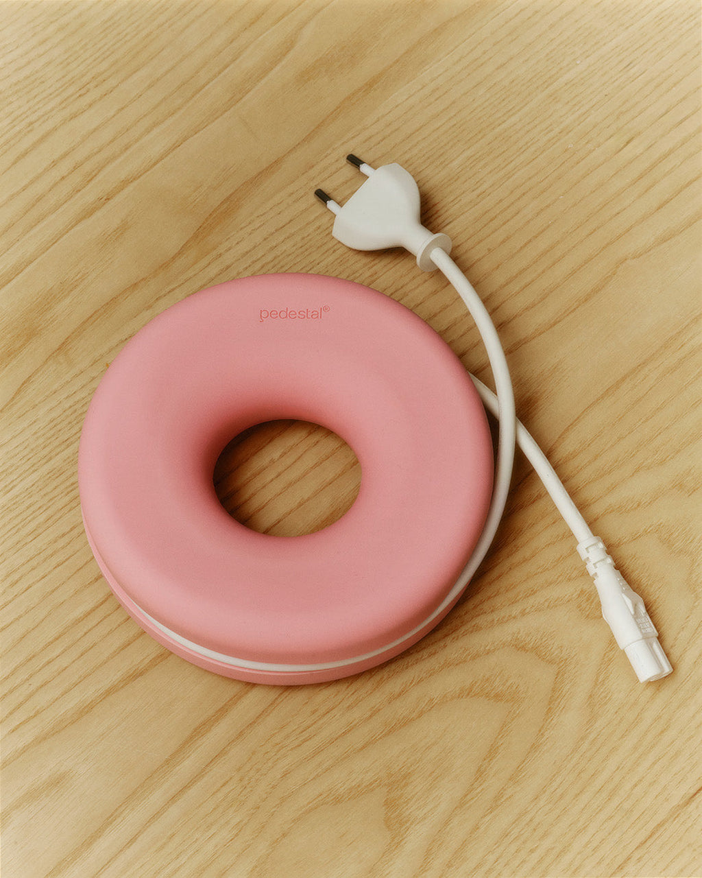 Pink Cable Bagel cable manager on light oak wood, white power cord wrapped around and plug ends extending out