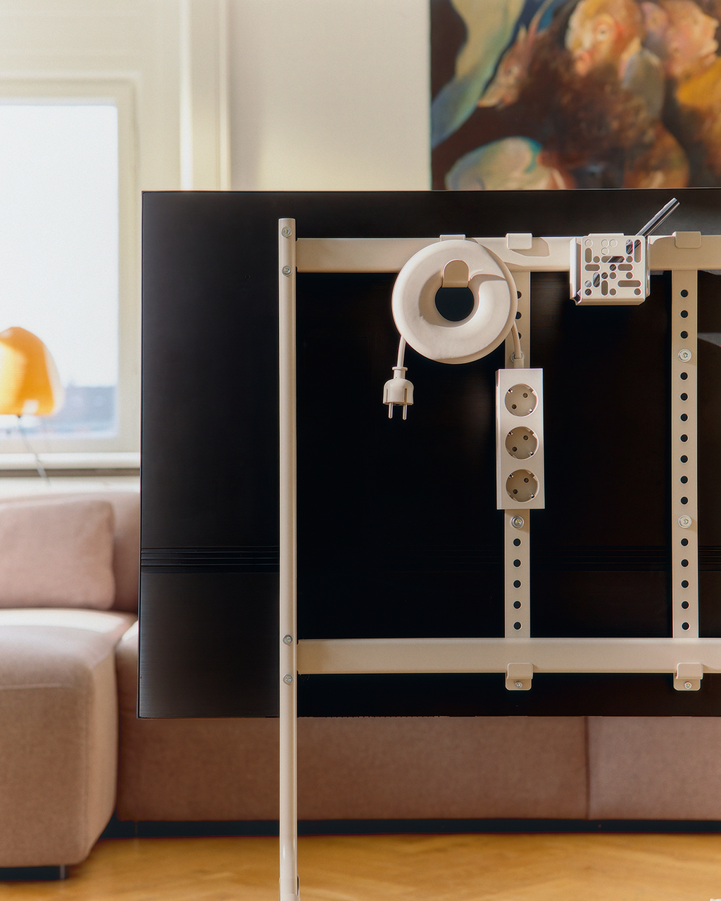 Oat Cable Bagel coiling a cord on a TV stand's rear frame in a living room, beside a power strip