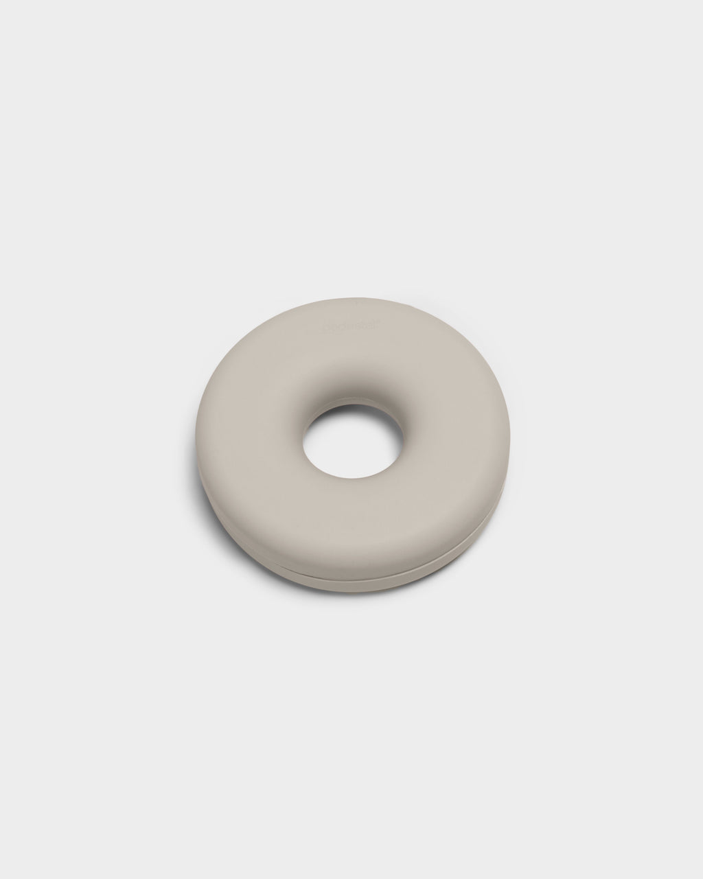 Cable Bagel cable manager in Oat, studio packshot angled view of the donut-shaped silicone disc with center hole