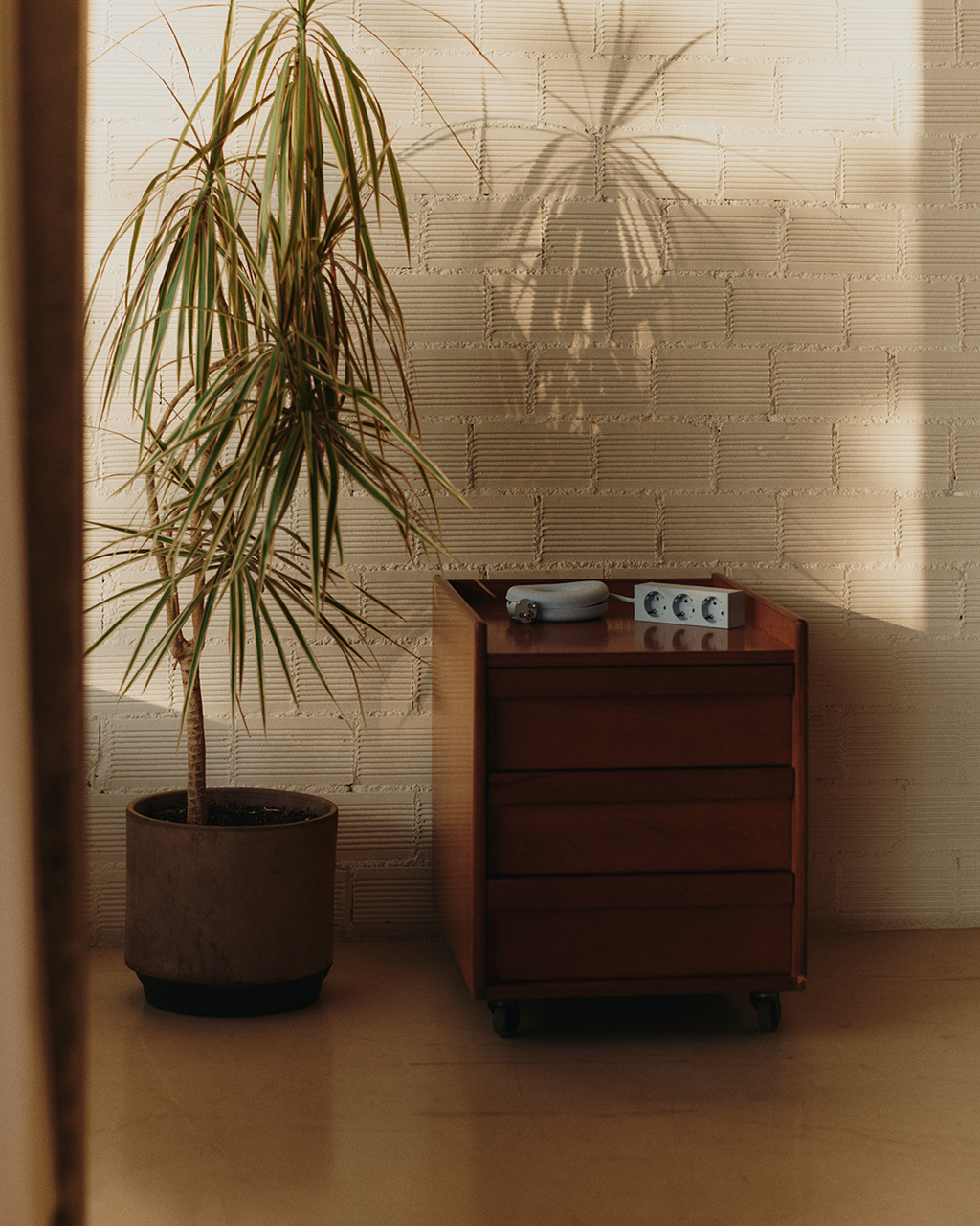 Powder Blue Cable Bagel coiling a power strip cord atop a wooden rolling drawer unit in a sunlit room with plant