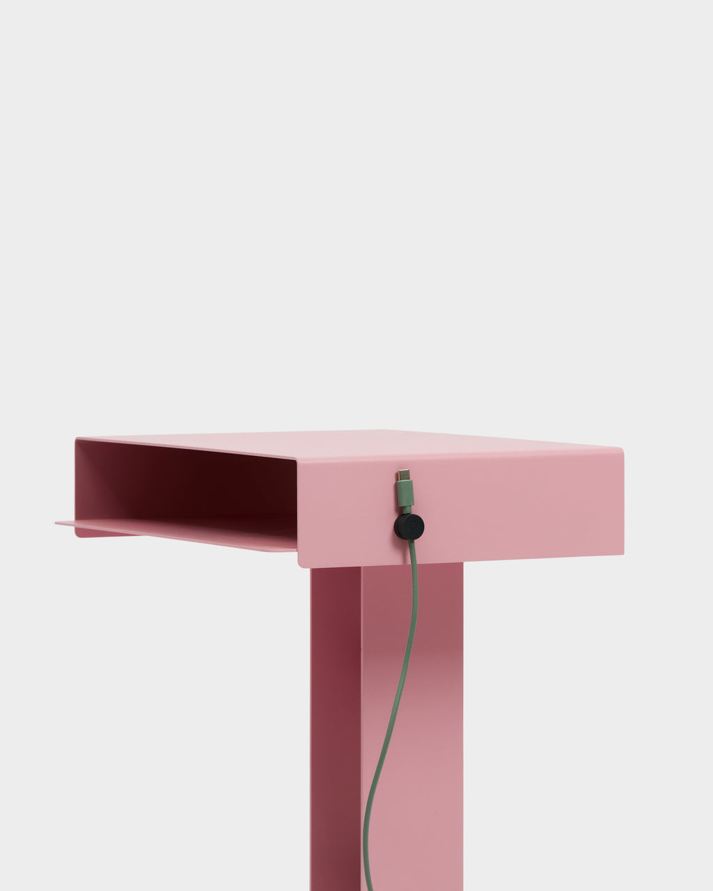 Charcoal Cable Clip holding a green cable against the side of a pink side table in a bright studio setting