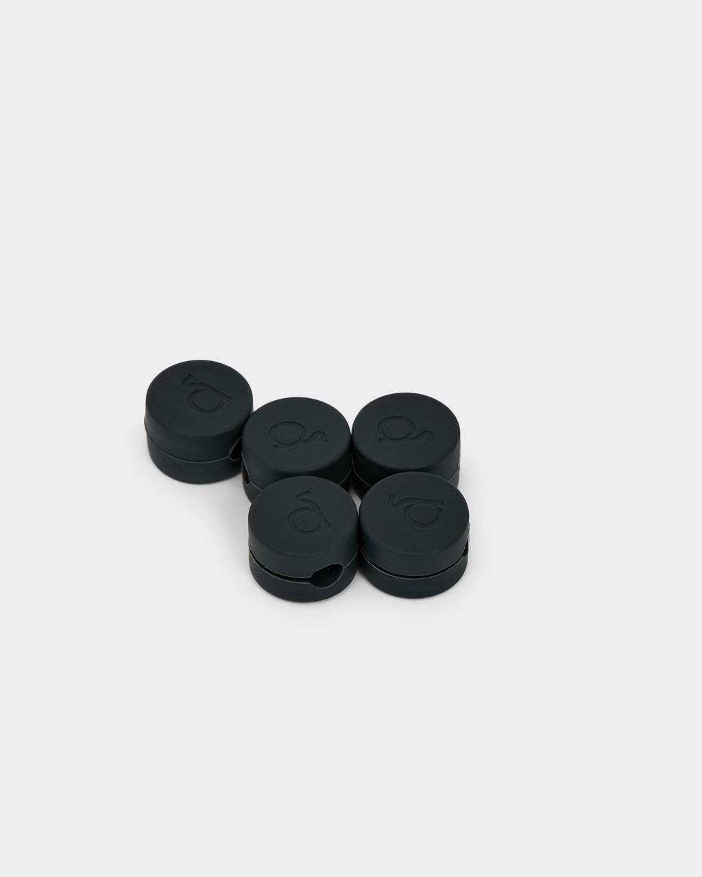 Five round charcoal Cable Clips arranged on a light grey studio backdrop, shown at an angle with embossed logo tops