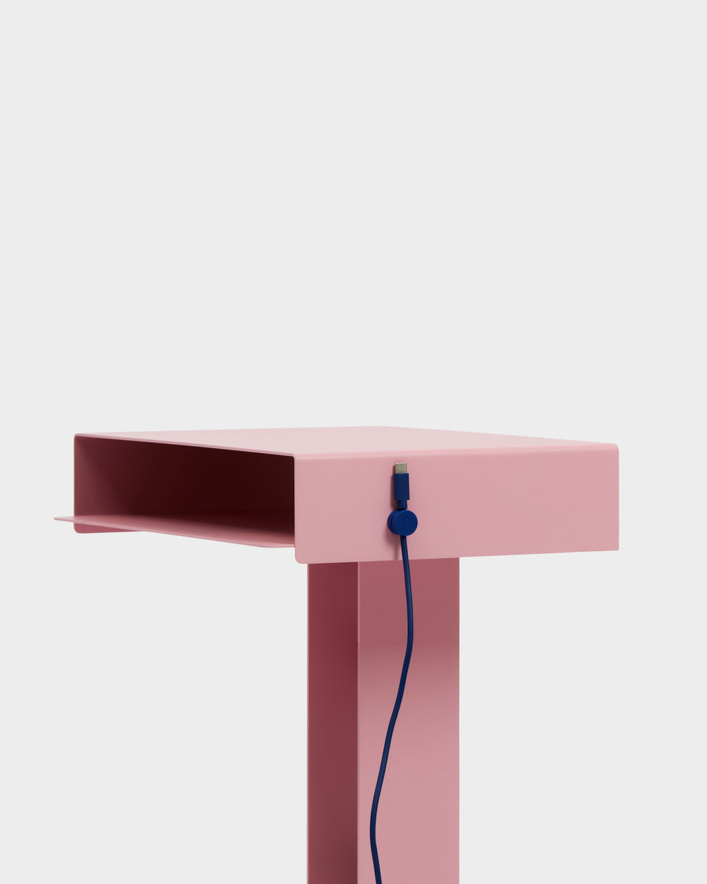 Ultra Marine Cable Clip holding a blue cord on a pink side table's edge, close-up studio shot