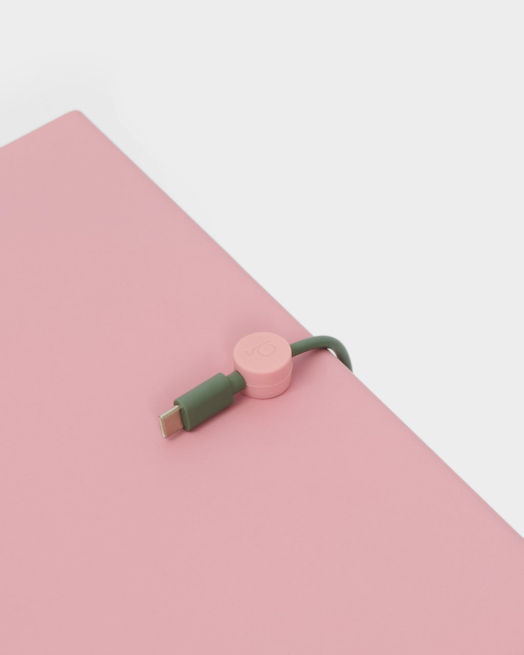 Bubble Gum Cable Clip holding a green USB-C cable at the edge of a pink desk, close-up studio angle