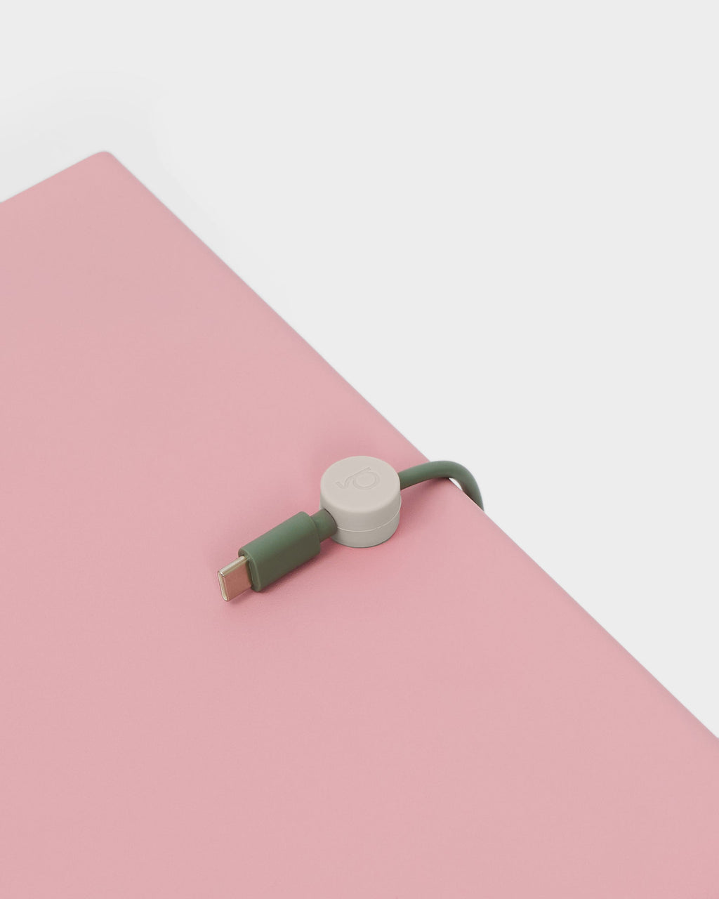 Oat Cable Clip holding a green USB-C cable at the edge of a pink desk, close-up angled studio shot
