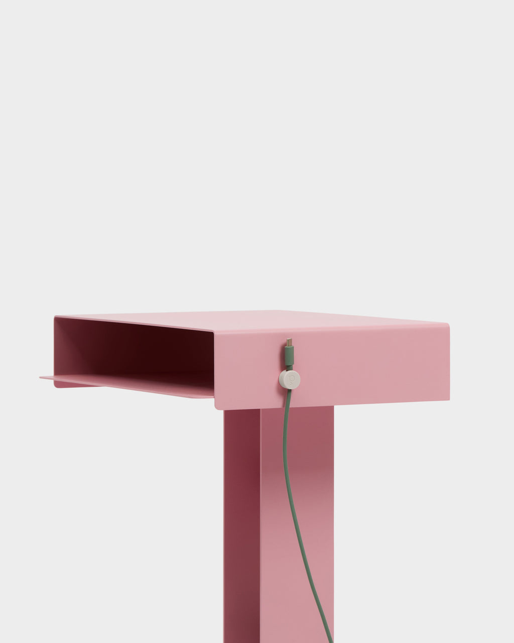 Oat Cable Clip holding a green cable against a pink side table's edge in a bright studio close-up