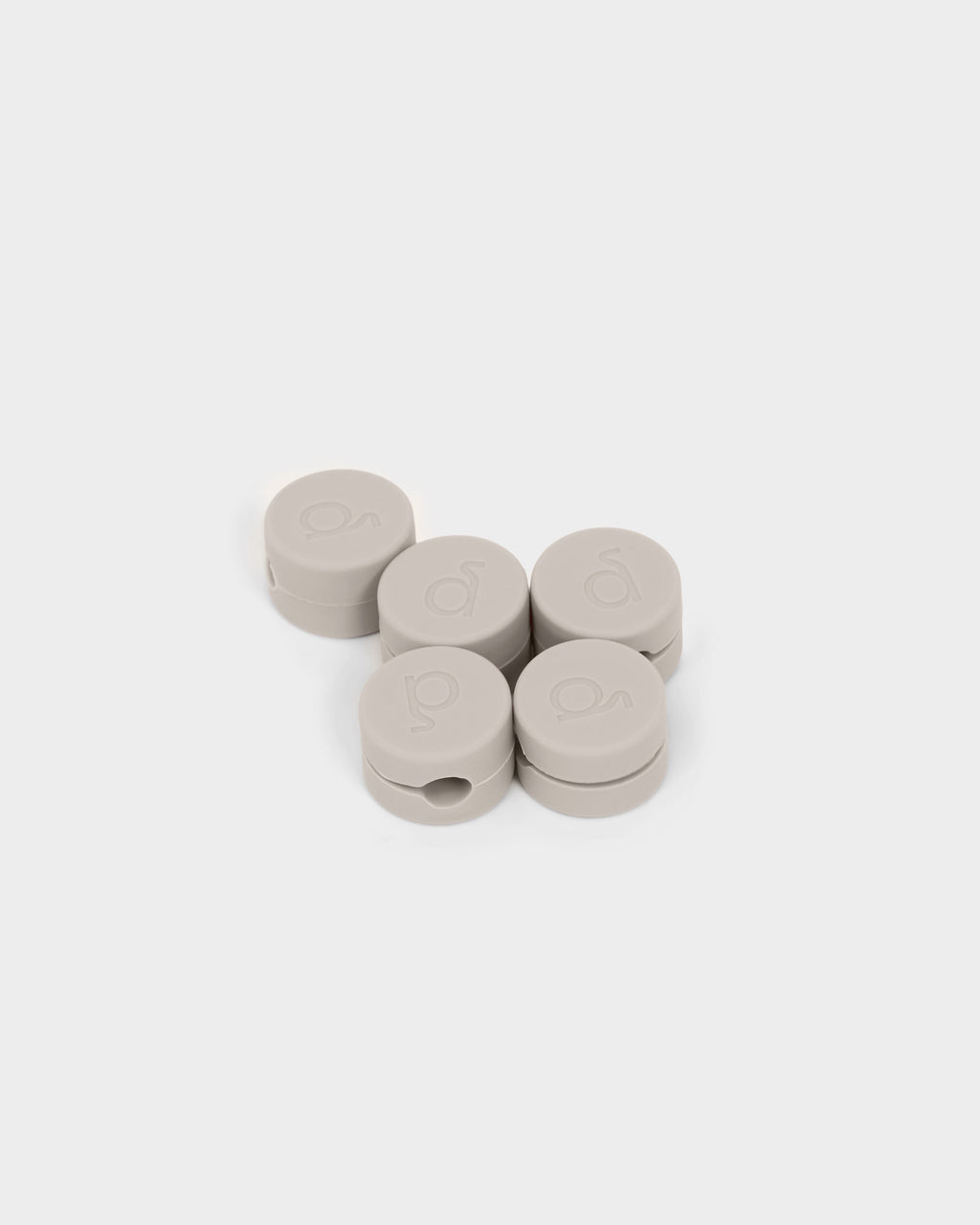 Five round Cable Clips in Oat with embossed logos, grouped on a white studio background at a slight angle