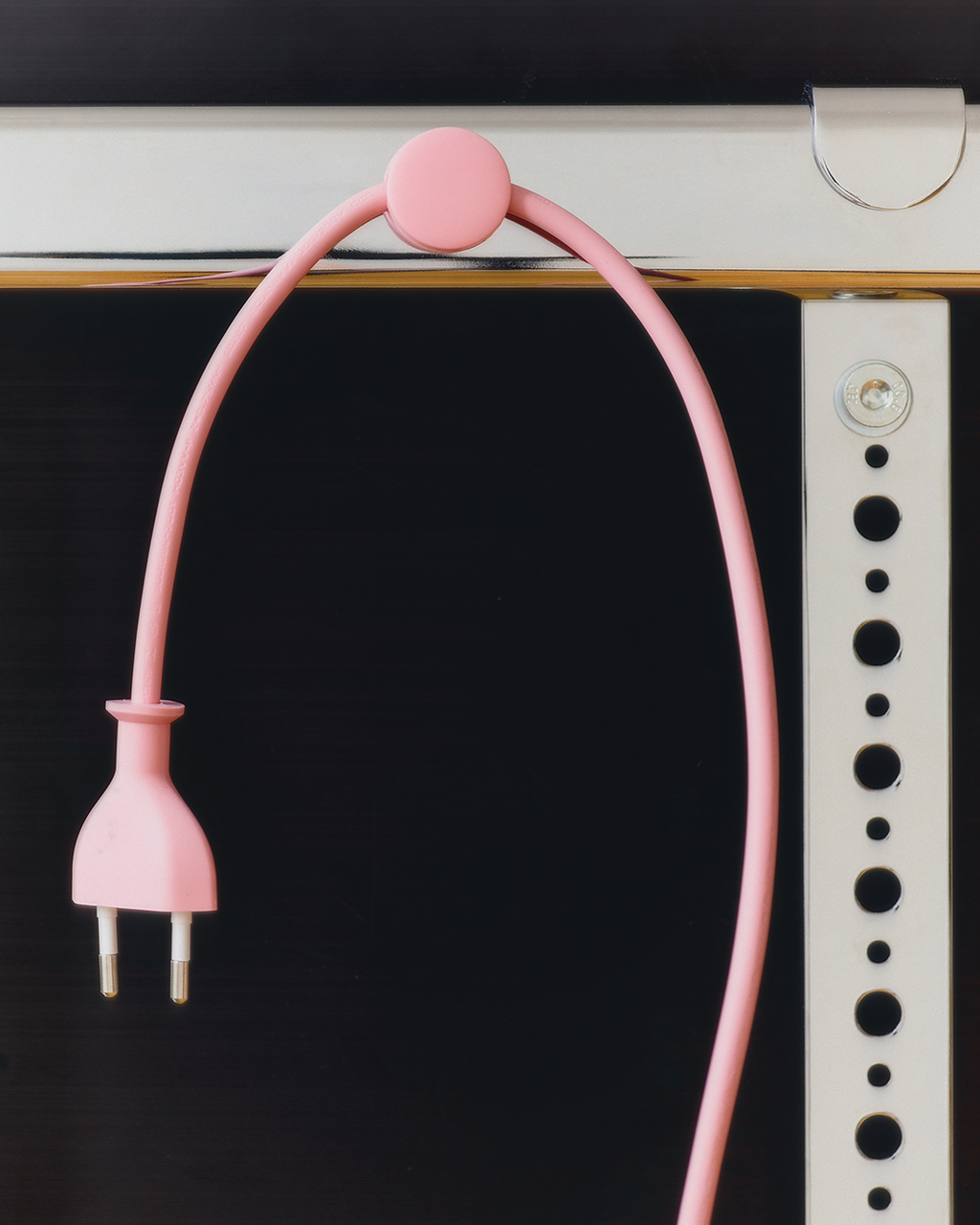 Pearl Cable Dot holding a pink power cord in an arc over a desk edge, plug dangling in a close studio shot