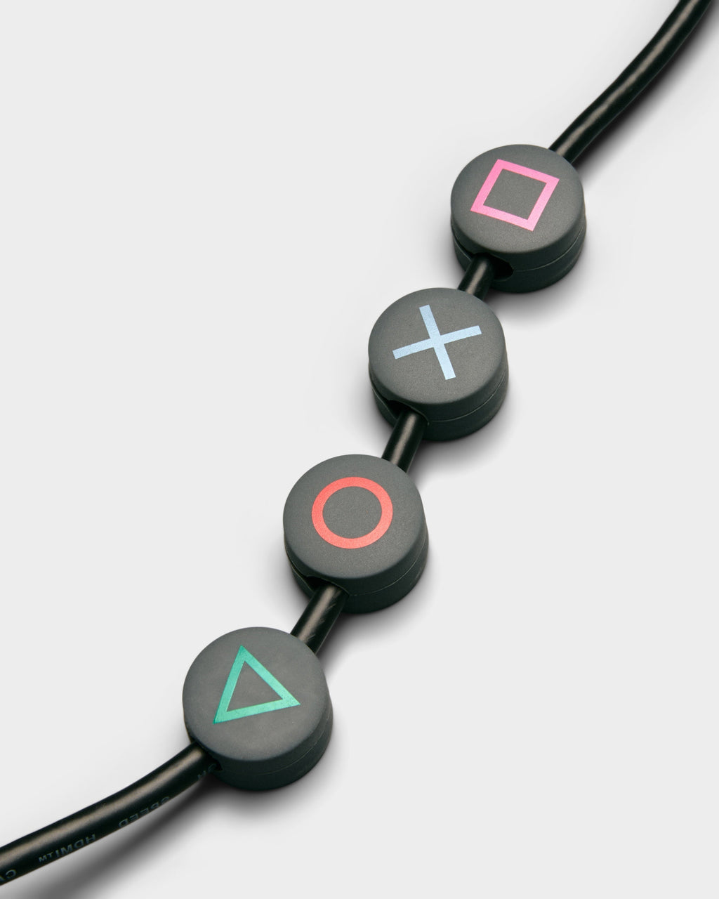 Four Cable Dots in Legacy Gray clipped along a black cable, studio packshot with pink, blue, red, green symbols