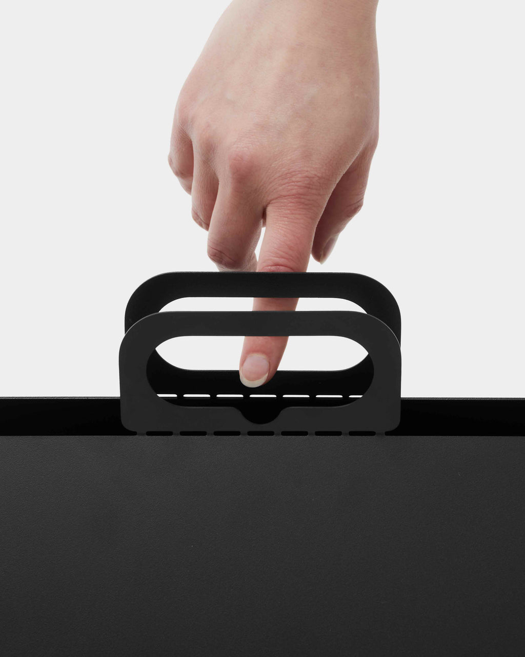 Hand lifting the Cable House in Charcoal by its slotted carry handle, close-up studio detail on white