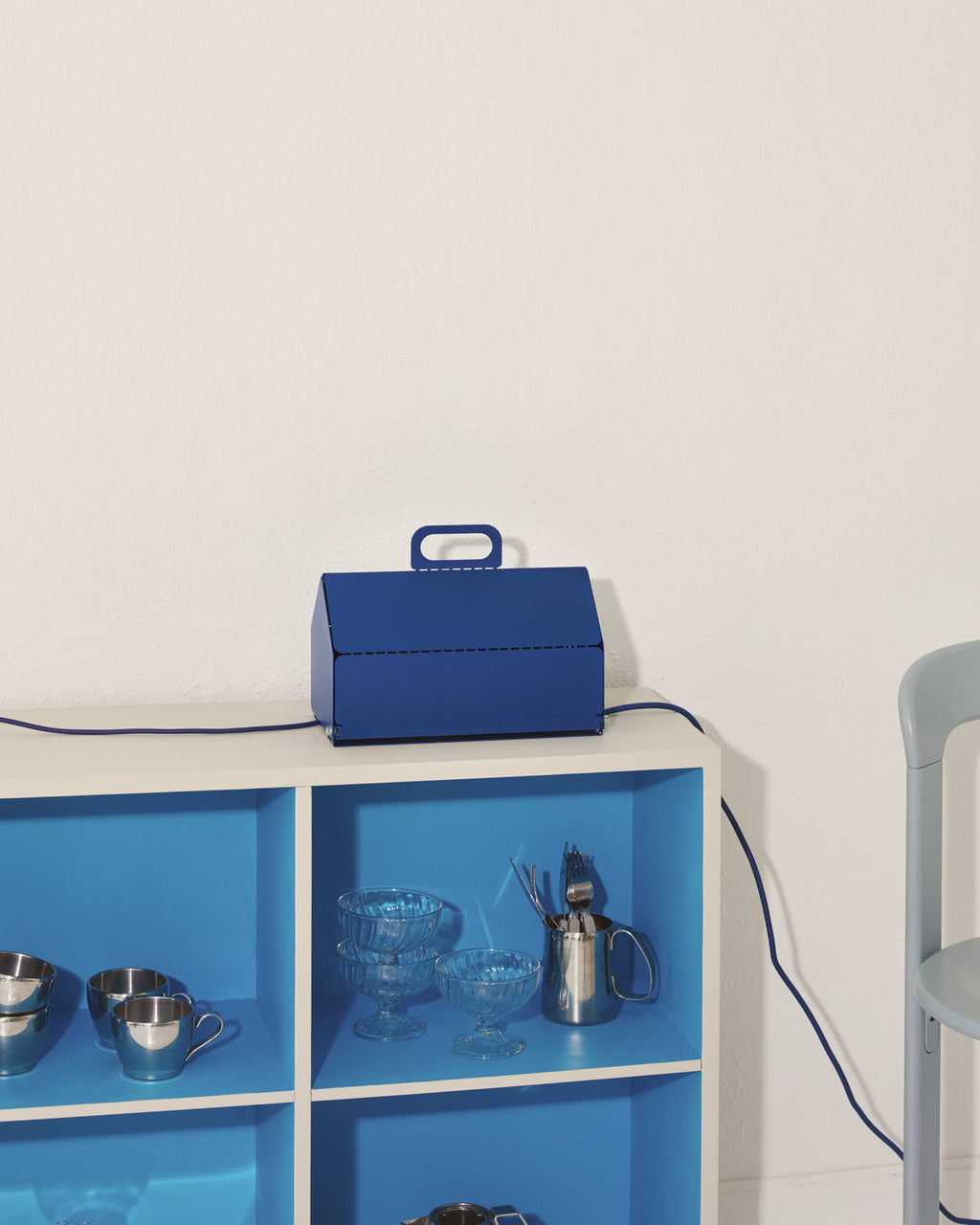 Ultra Marine Cable House sitting atop a white shelving unit, blue cord trailing down past glassware in lit blue cubbies