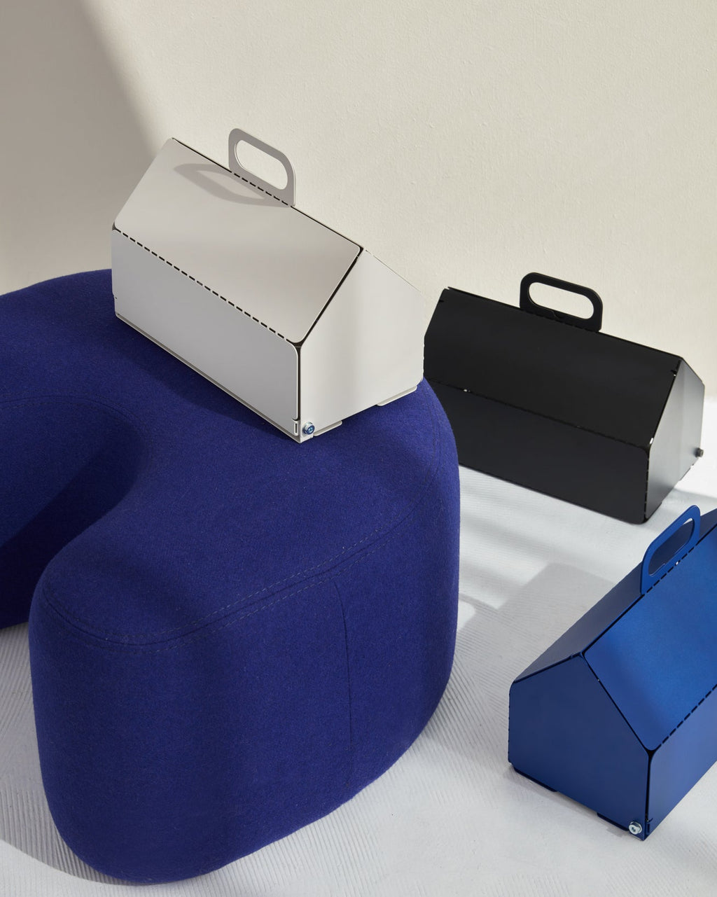 Cable House in Ultra Marine alongside white and black versions, styled with a blue wool pouf in a bright studio scene