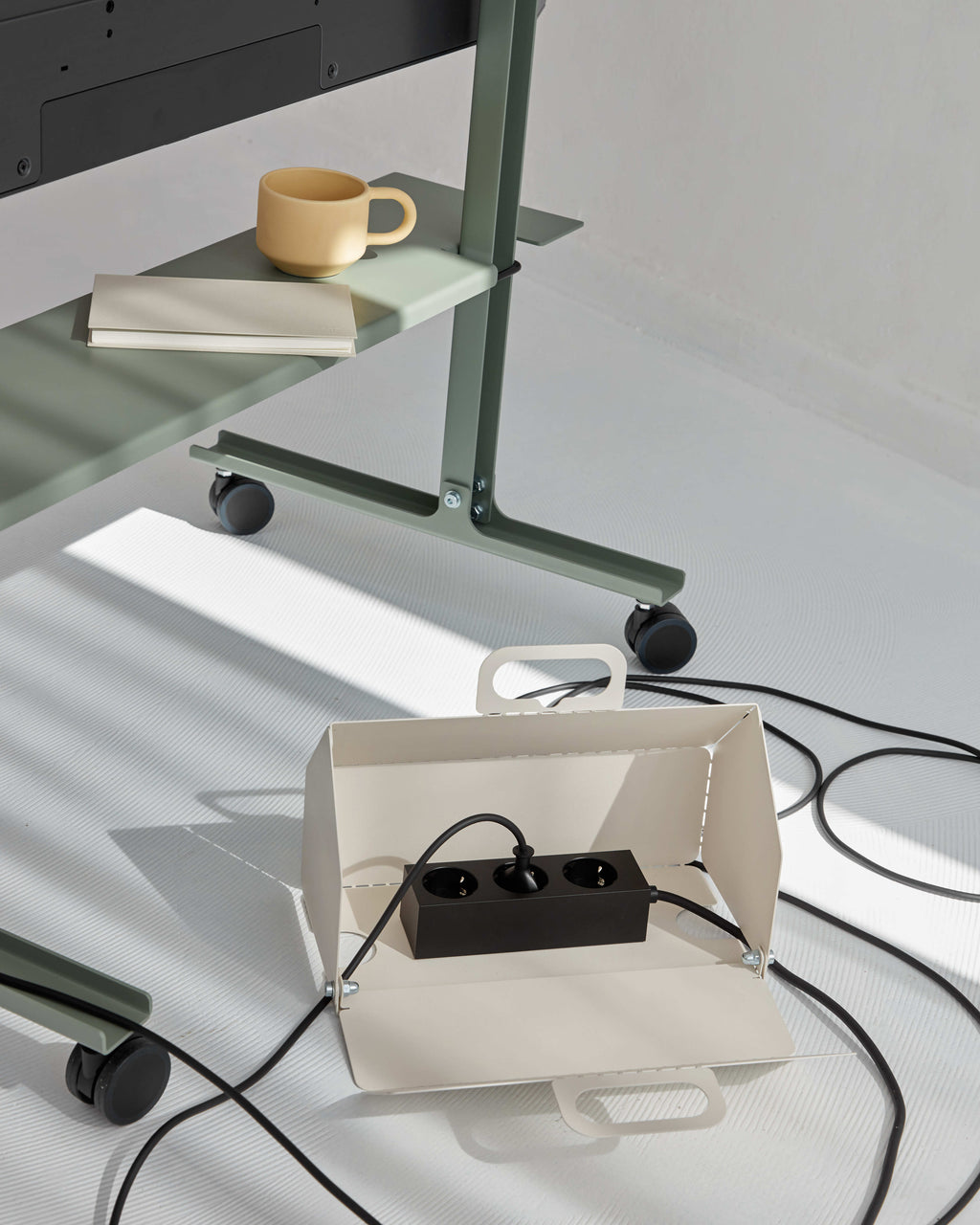 Pearl Cable House open on a sunlit floor beside a green rolling desk, holding a black power strip with cords running out