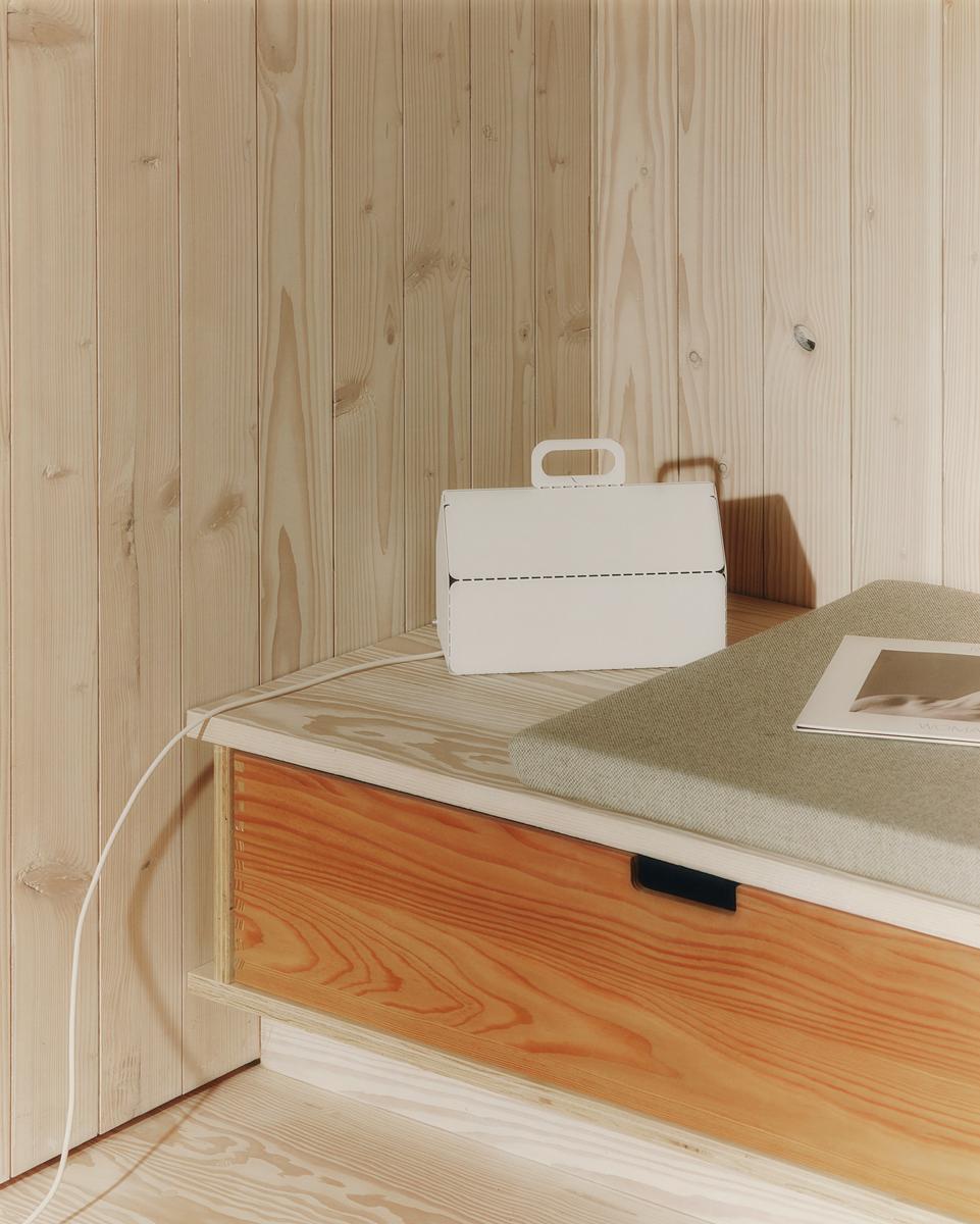 Cable House in Pearl on a plywood bench in a pine-clad room, white cord trailing down to the floor