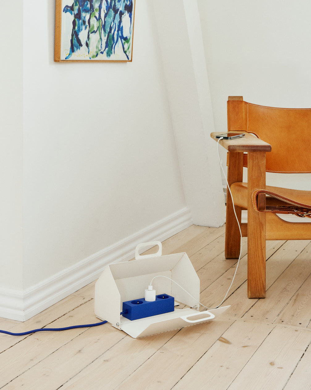 Pearl Cable House open on wood floor, holding a blue power strip and charger beside a leather lounge chair