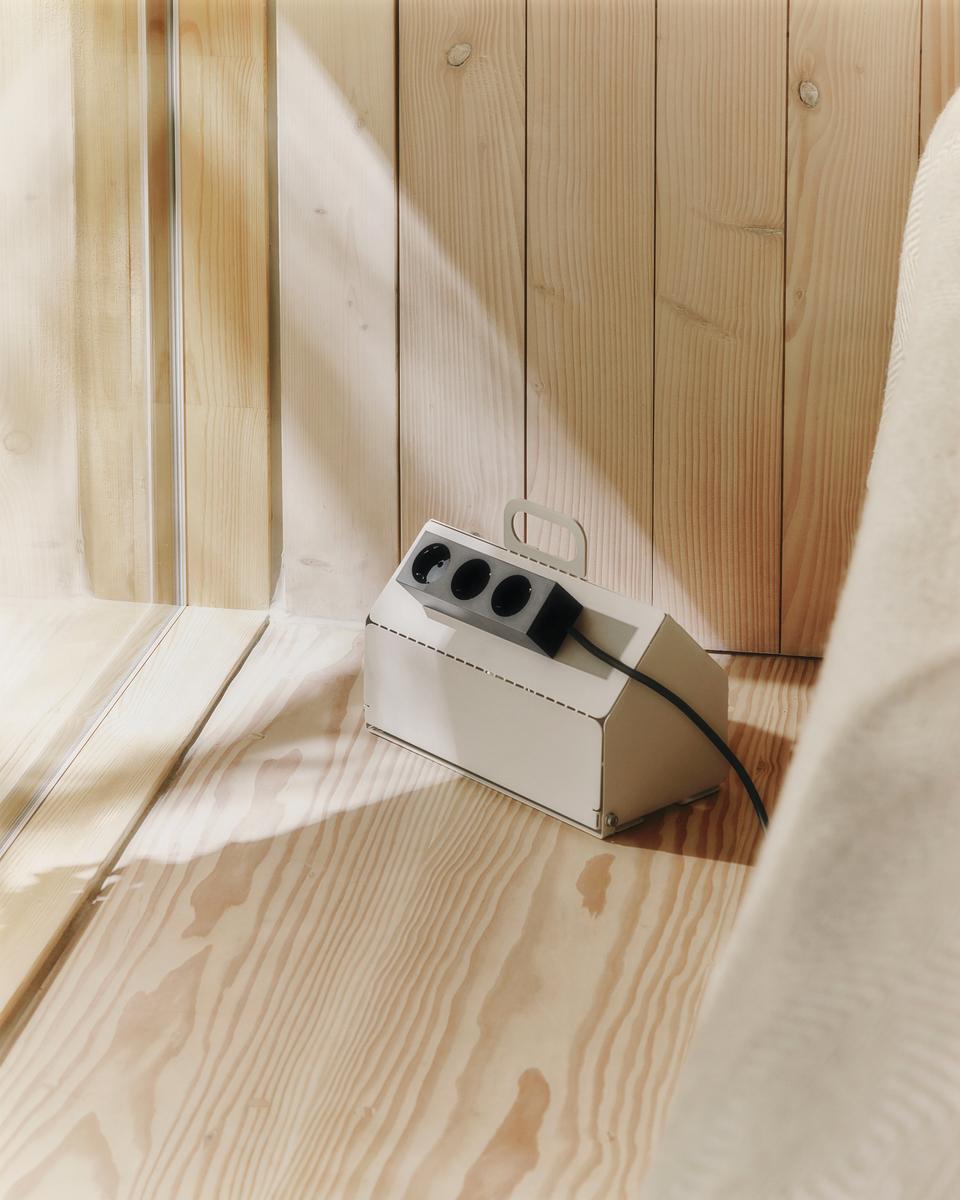 Pearl Cable House on a sunlit pine floor, angled view showing power strip and cable tucked inside its metal cover