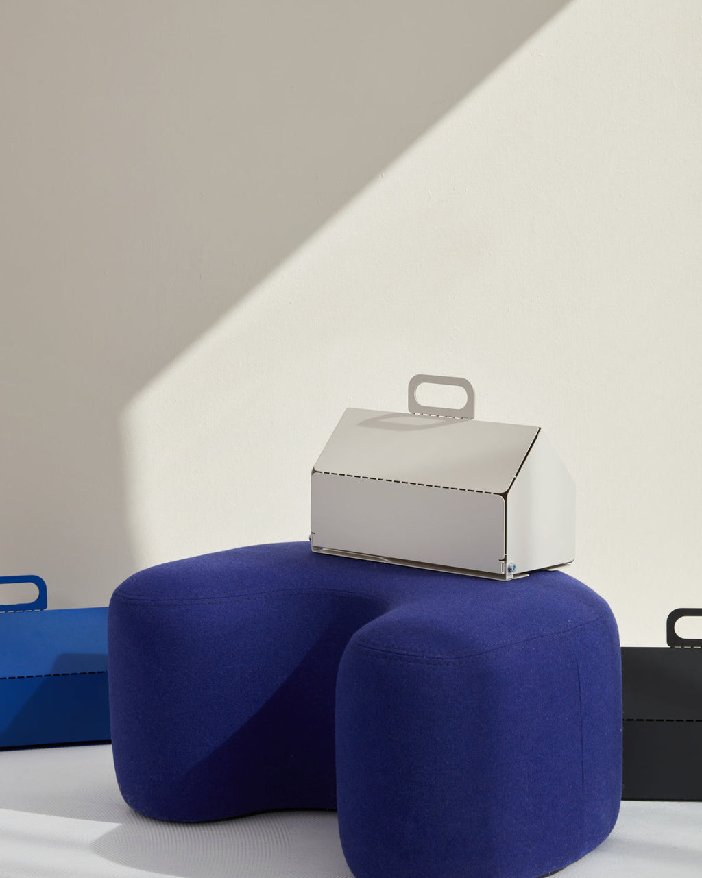 Pearl Cable House with carry handle sits on a blue wool pouf in a sunlit studio scene, angled front view
