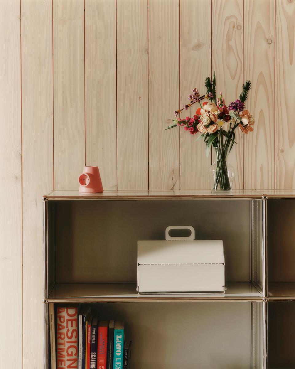 Pearl Cable House sits on a metal shelf below a pine wall, with flowers and a coral lamp styled above