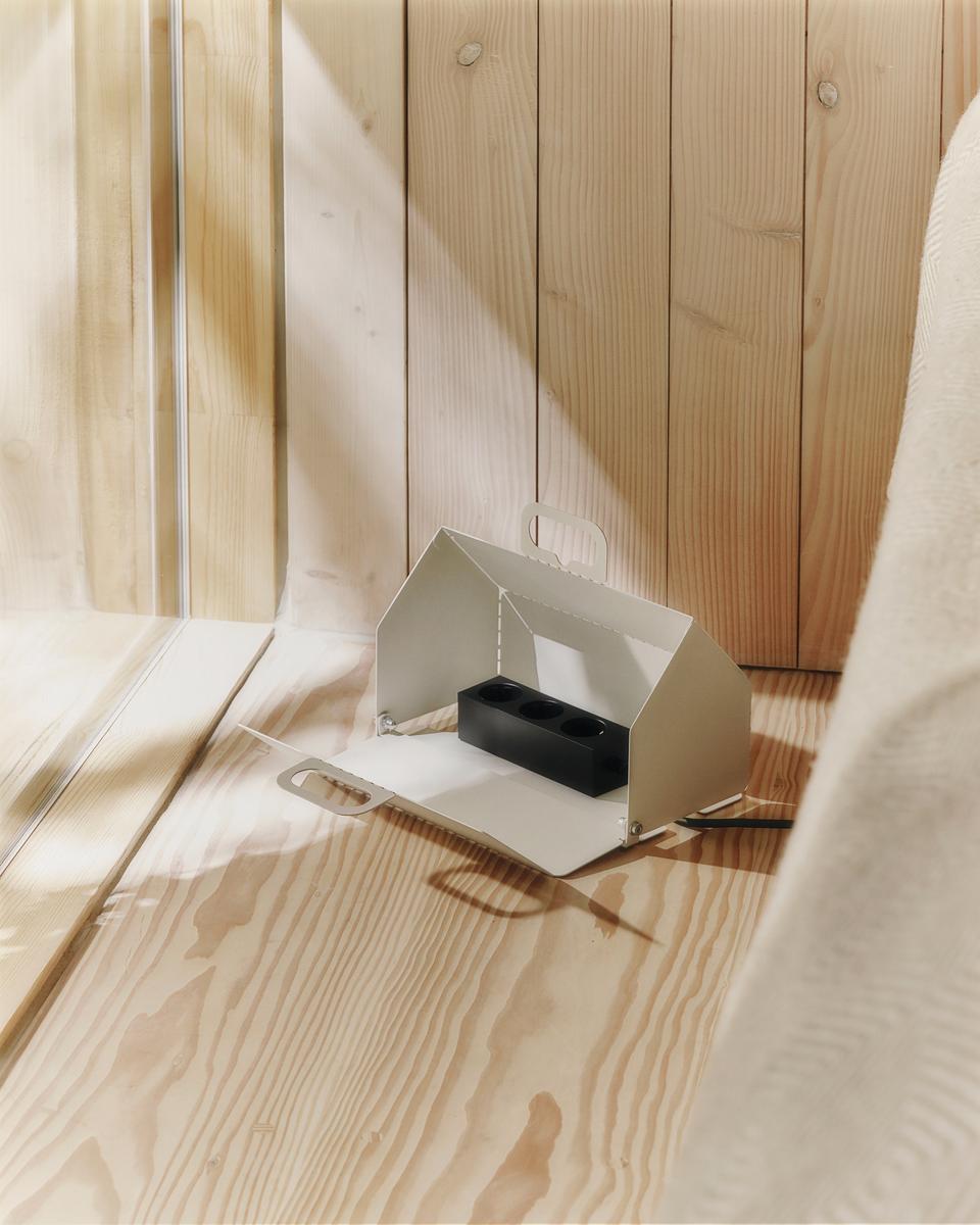 Pearl Cable House open on a sunlit pine floor, revealing a black power strip inside with cord trailing out