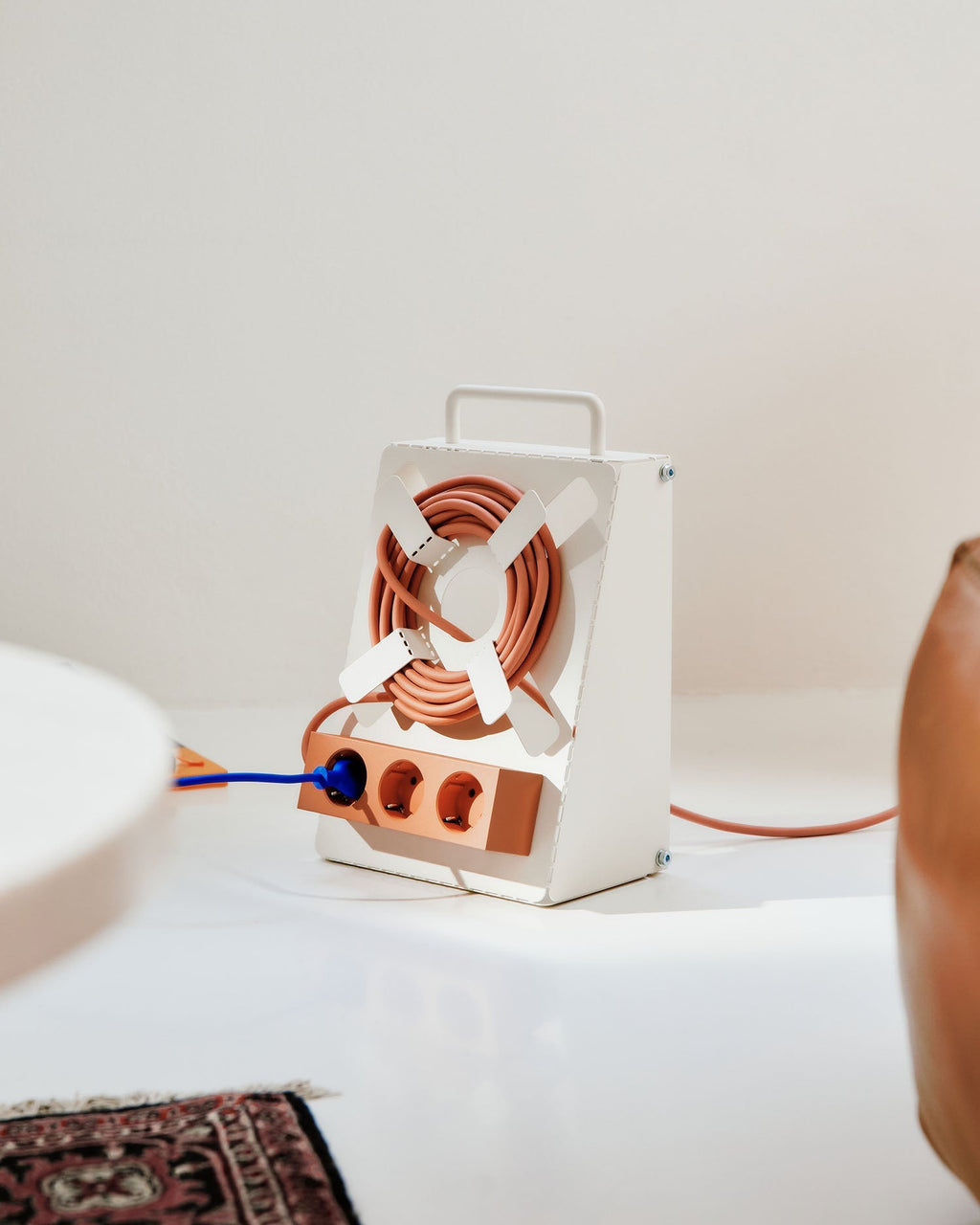 Cable Stand in Charcoal on a white table, coiled terracotta cord wound around its cross reel with a blue plug inserted