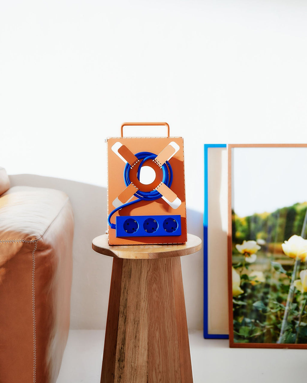 Dusty Rose Cable Stand with blue cable and socket strip on a wooden stool beside a leather sofa and framed prints
