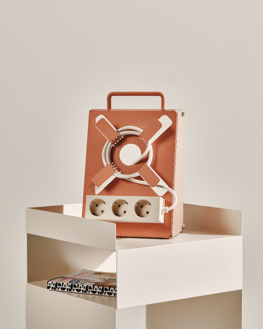 Dusty Rose Cable Stand with wrapped white cord and three-socket strip, sitting on a cream side table by magazines