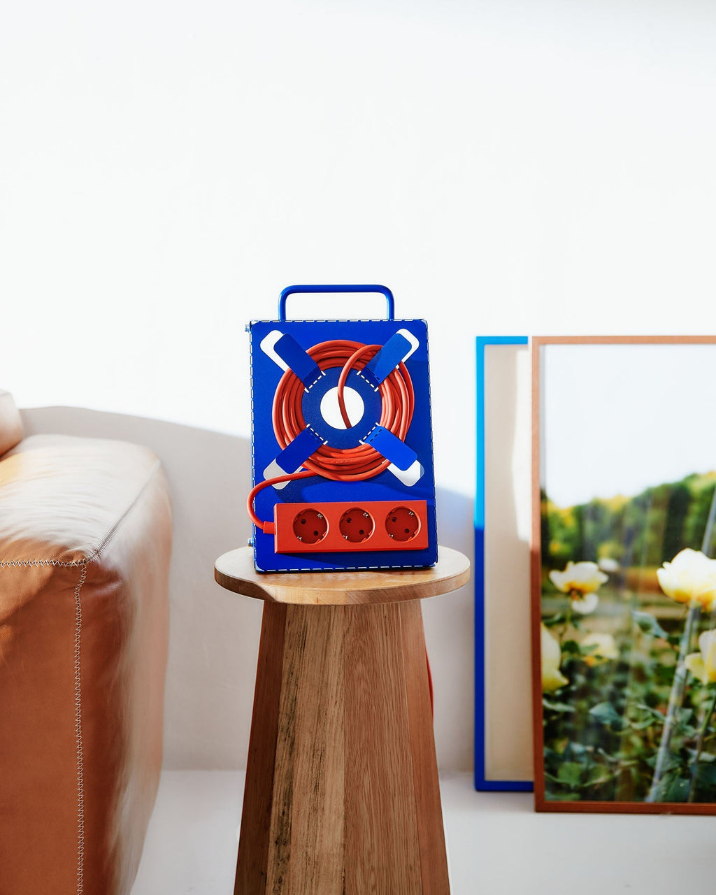 Ultra Marine Cable Stand with coiled red cord on a wooden stool beside a leather sofa and framed floral print