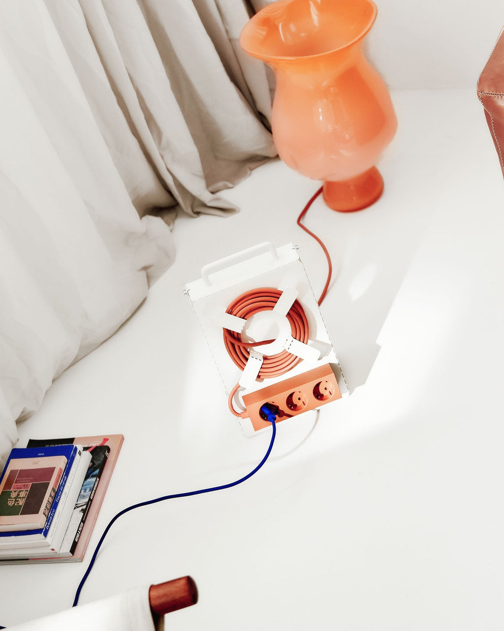 Pearl Cable Stand holding coiled orange cord beside a glass lamp and stacked books in a sunlit bedroom scene