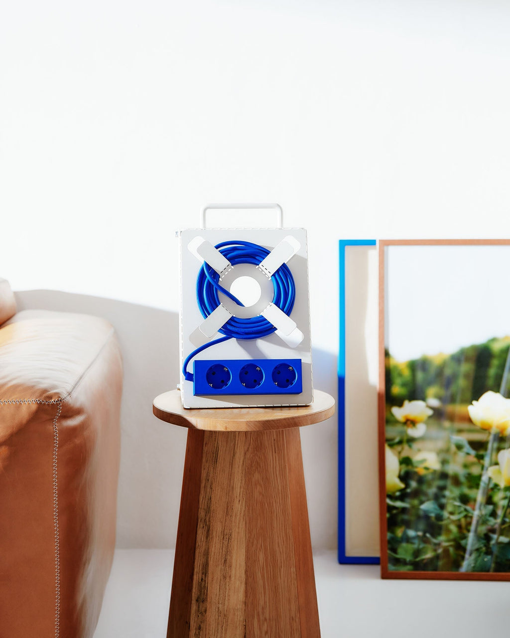 Pearl Cable Stand on a wooden side table in a living room, blue cord coiled around its cross-shaped holder