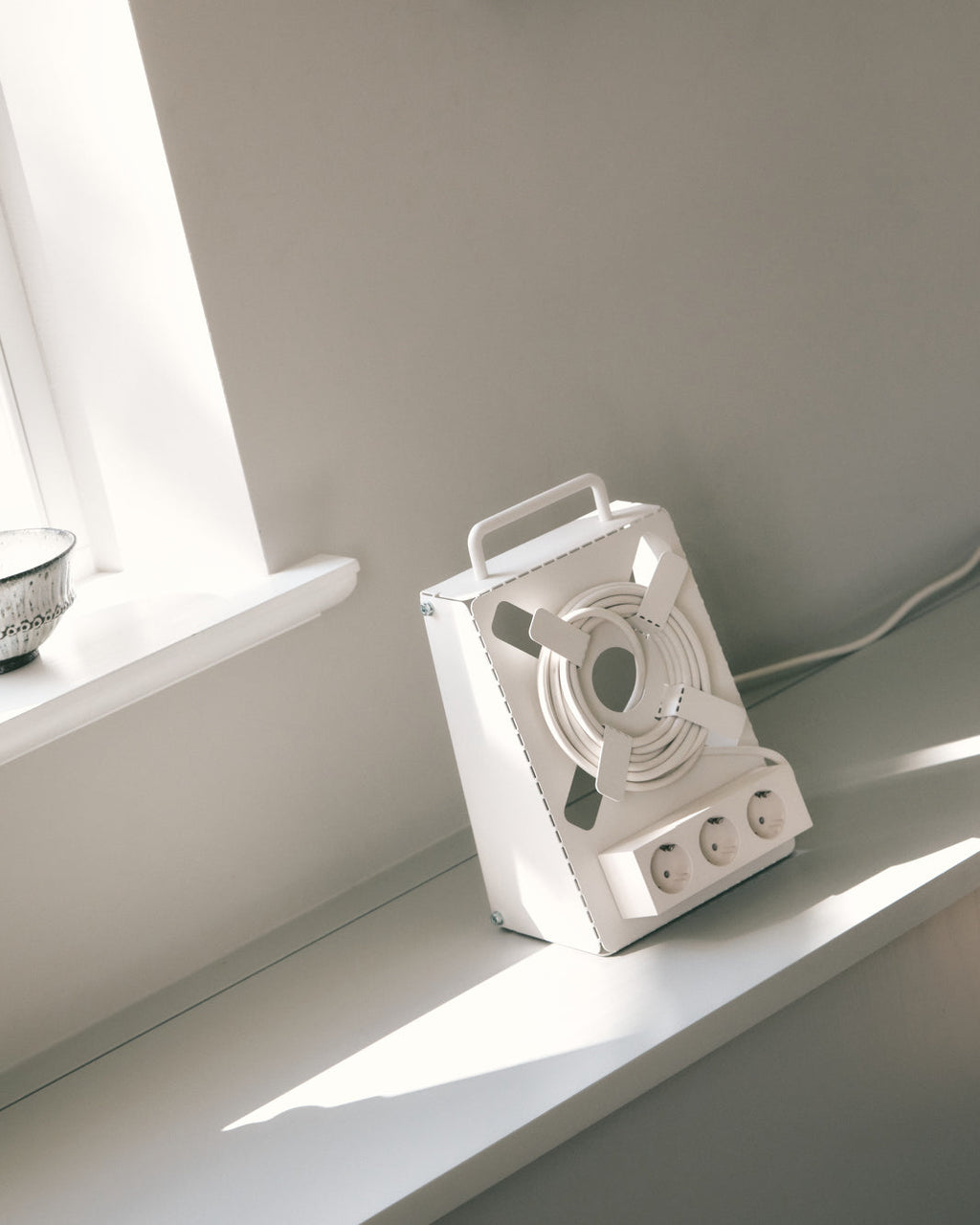 Pearl Cable Stand with coiled cord and three sockets resting on a sunlit windowsill ledge in a bright room
