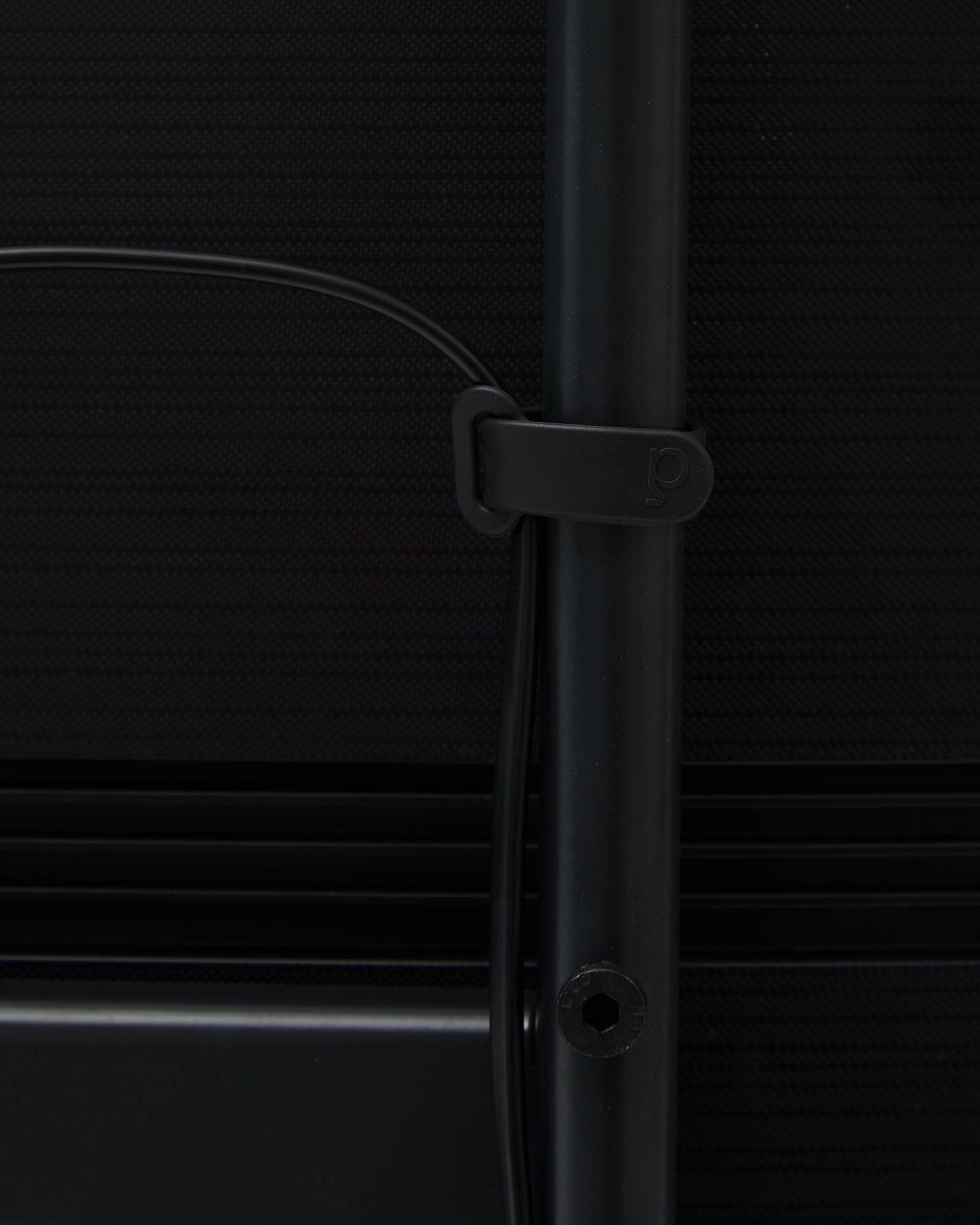 Close-up of charcoal Cable Tie wrapped around a black desk leg, holding cable neatly in place against dark panel