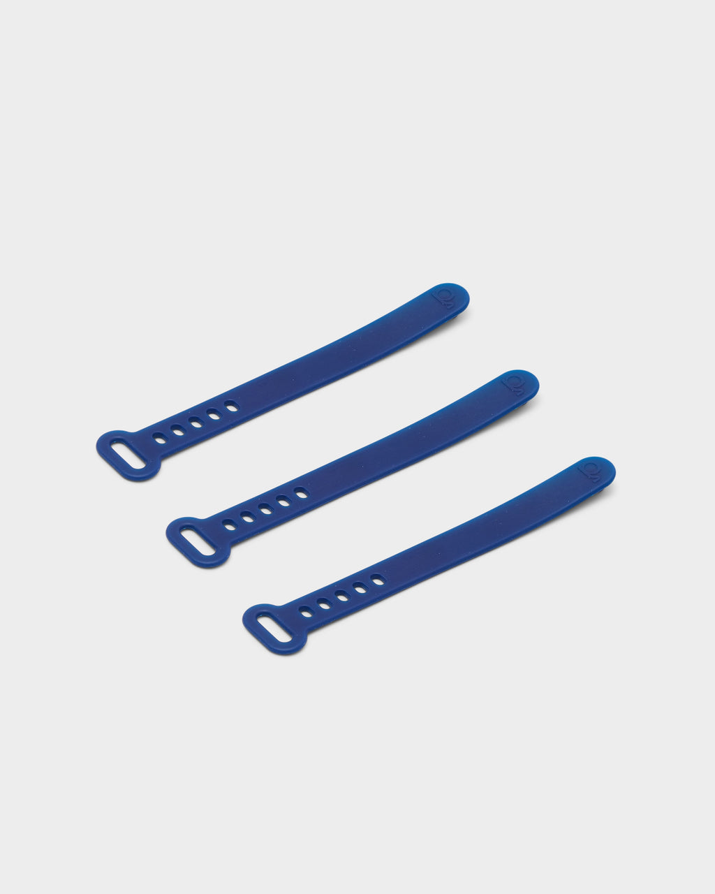 Three Ultra Marine silicone cable ties arranged diagonally on a light grey studio backdrop, showing slotted ends and holes