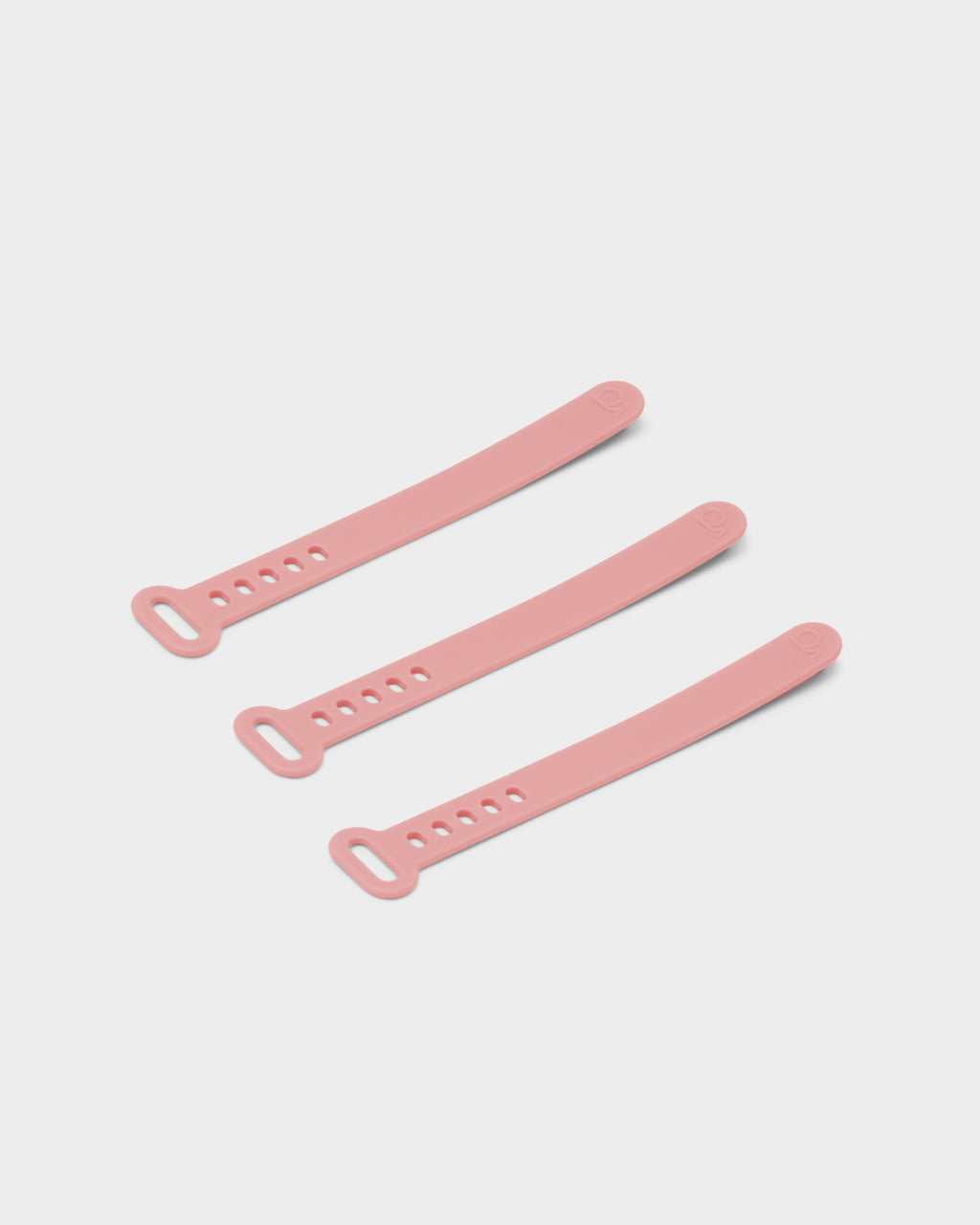 Three Bubble Gum pink silicone Cable Ties arranged diagonally on a light grey studio background, shown flat and unfastened